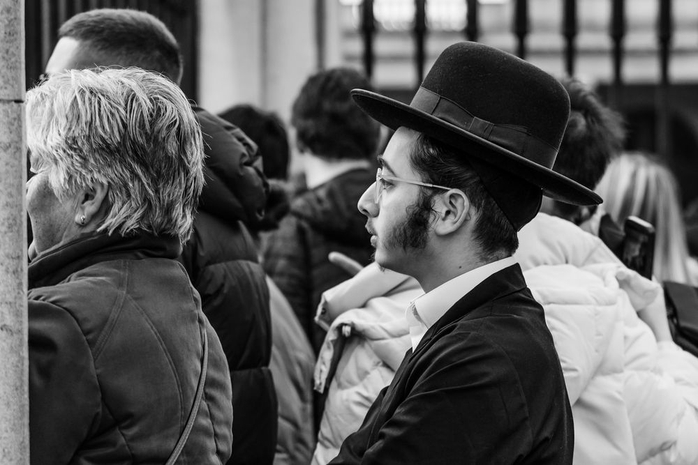 A black and white profile view of a person wearing a traditional wide-brimmed hat in a crowd.