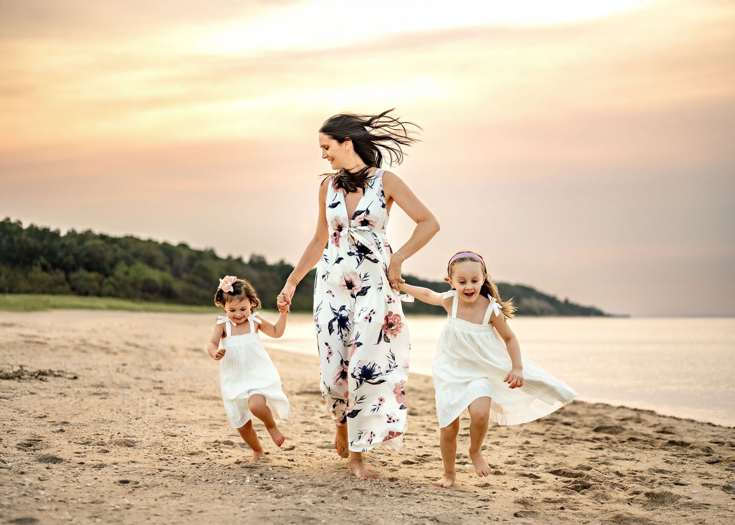 Family wearing white outfits runs and plays together on a sandy beach at sunset.