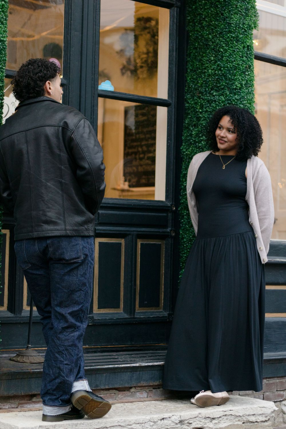 A couple interacts playfully outside a storefront with green ivy decor.