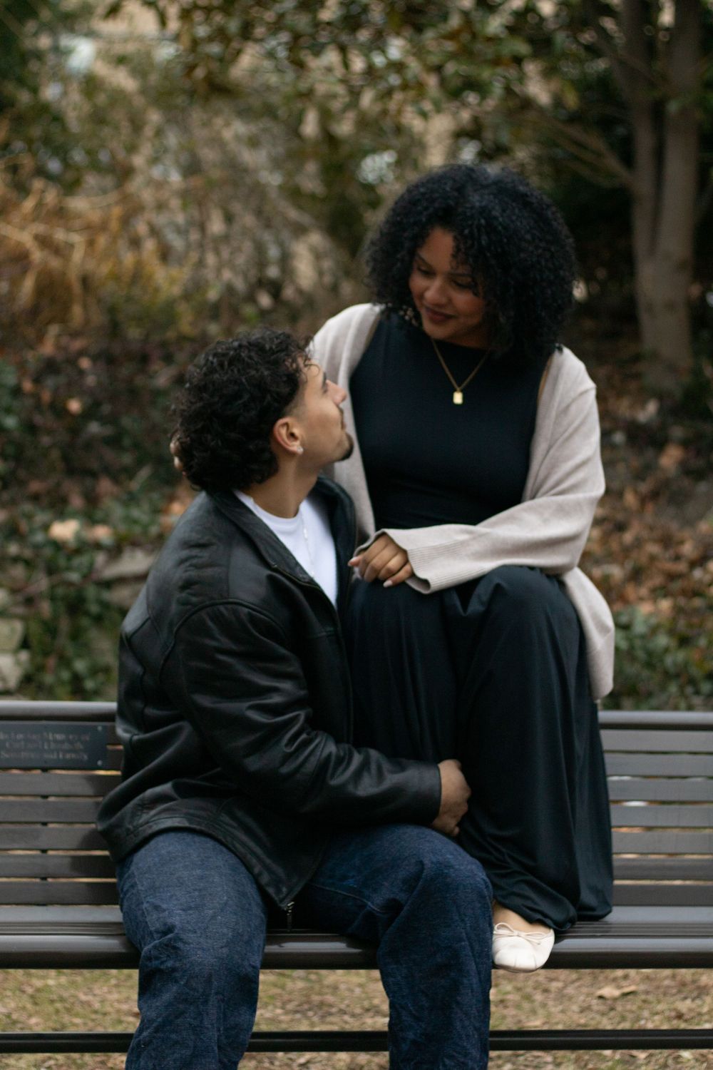 Two people share a sweet moment while sitting together on a wooden park bench.