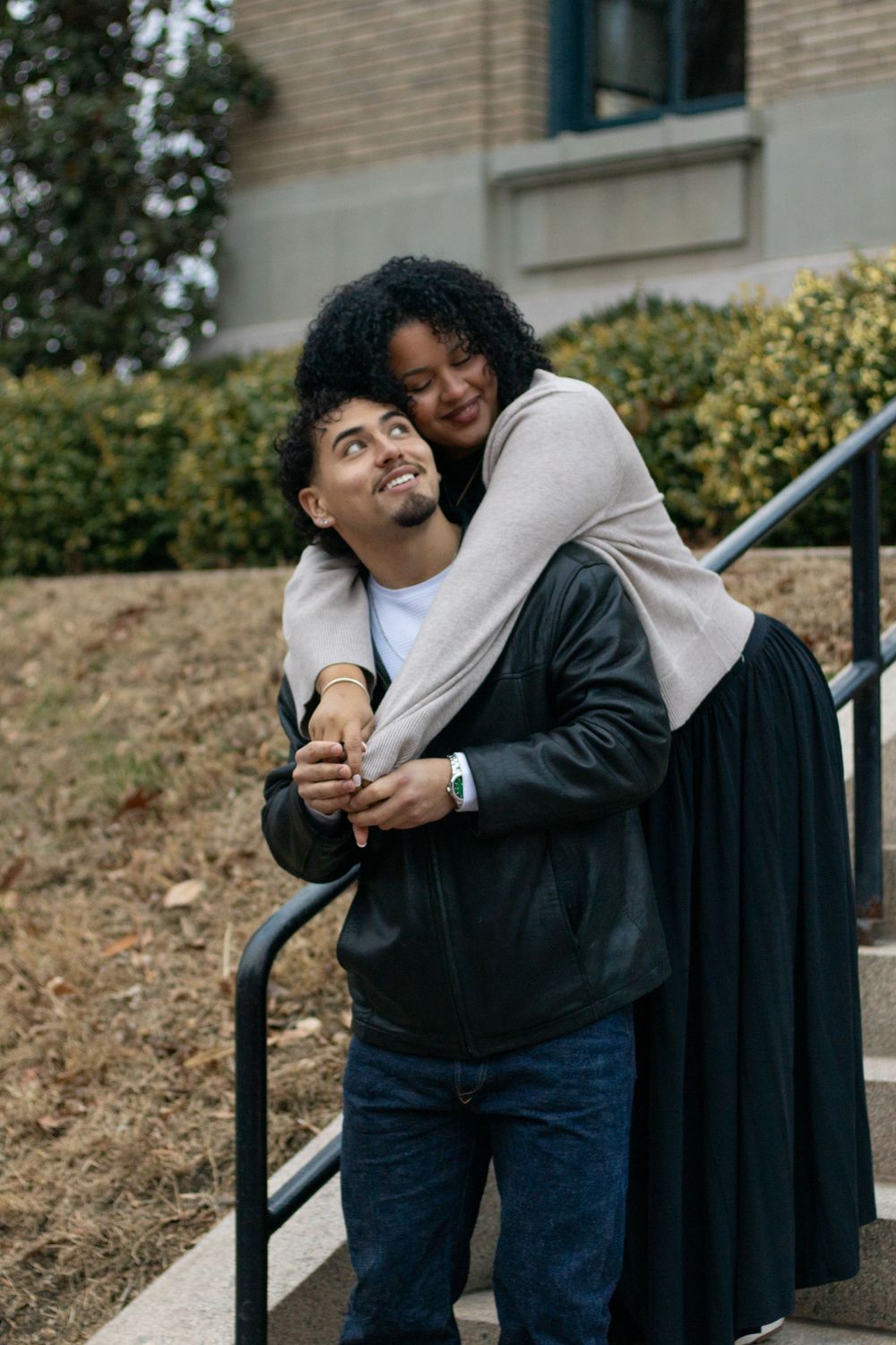 A couple shares an affectionate moment on outdoor steps near brick buildings.