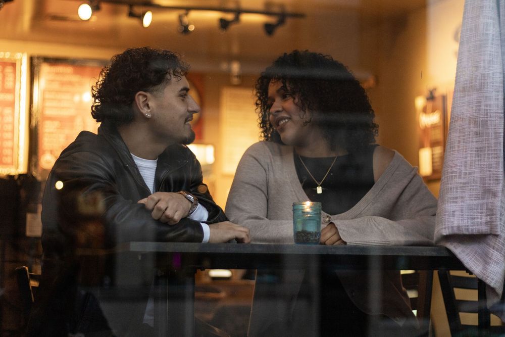 Couple sits at a cozy restaurant table with warm lighting and brick walls in the background.
