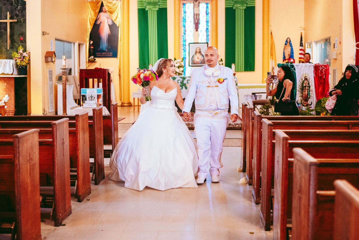 Wedding ceremony in a traditional church with green shutters and wooden pews decorated in white and gold decor.