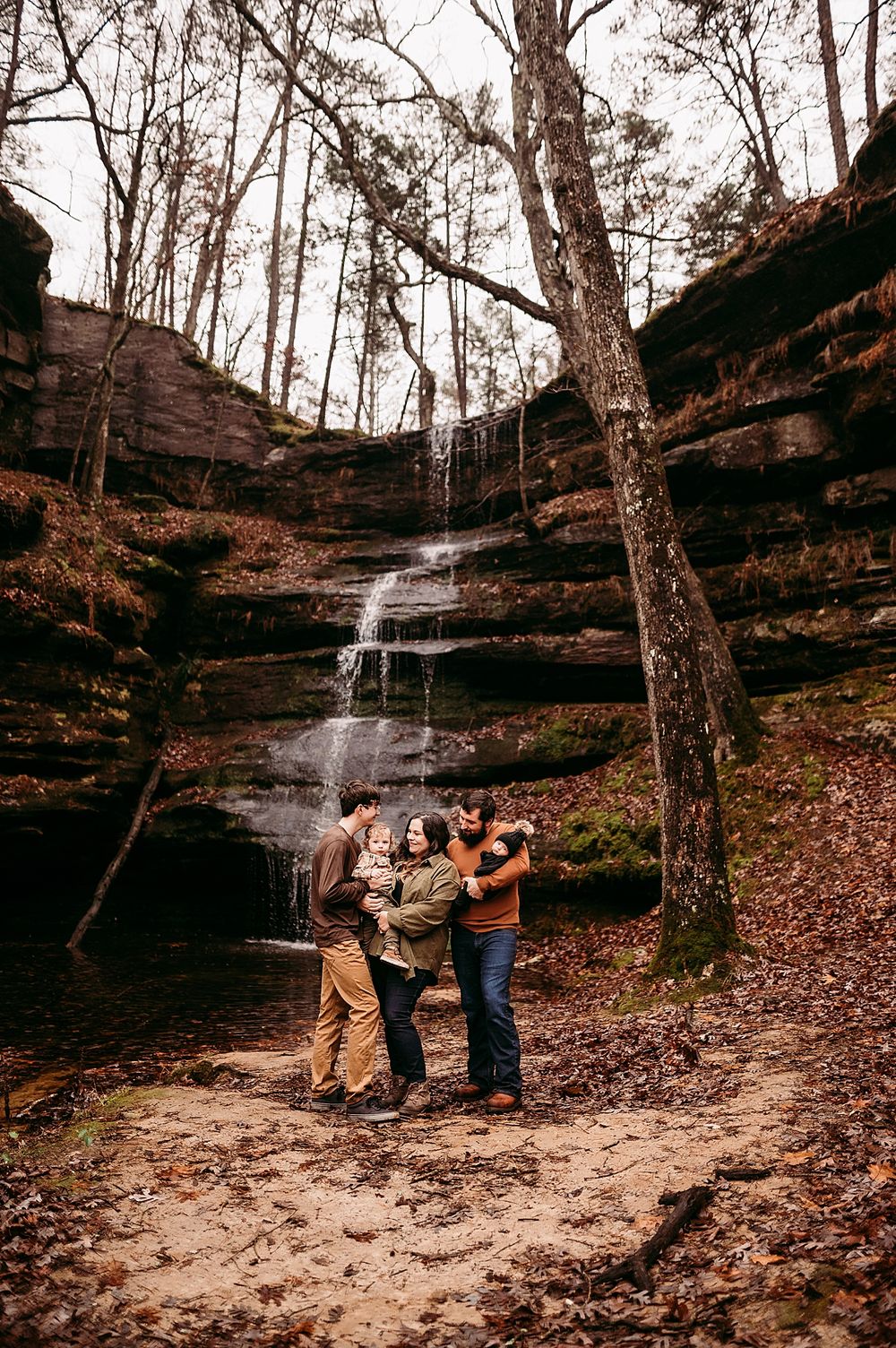 Group enjoying nature at scenic waterfall cascading down rocky cliff through autumn forest.