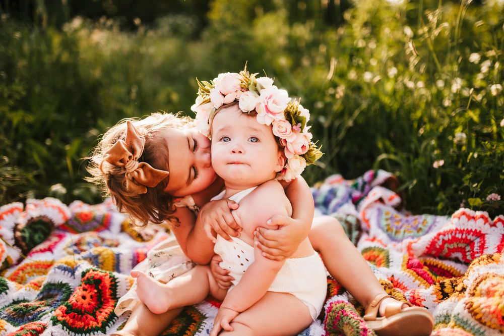 Sweet floral crown moment captured on picnic blanket in sunny meadow with colorful quilts.