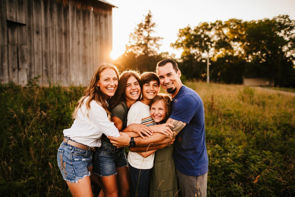 Warm sunset light illuminates a group hug against rustic barn backdrop.