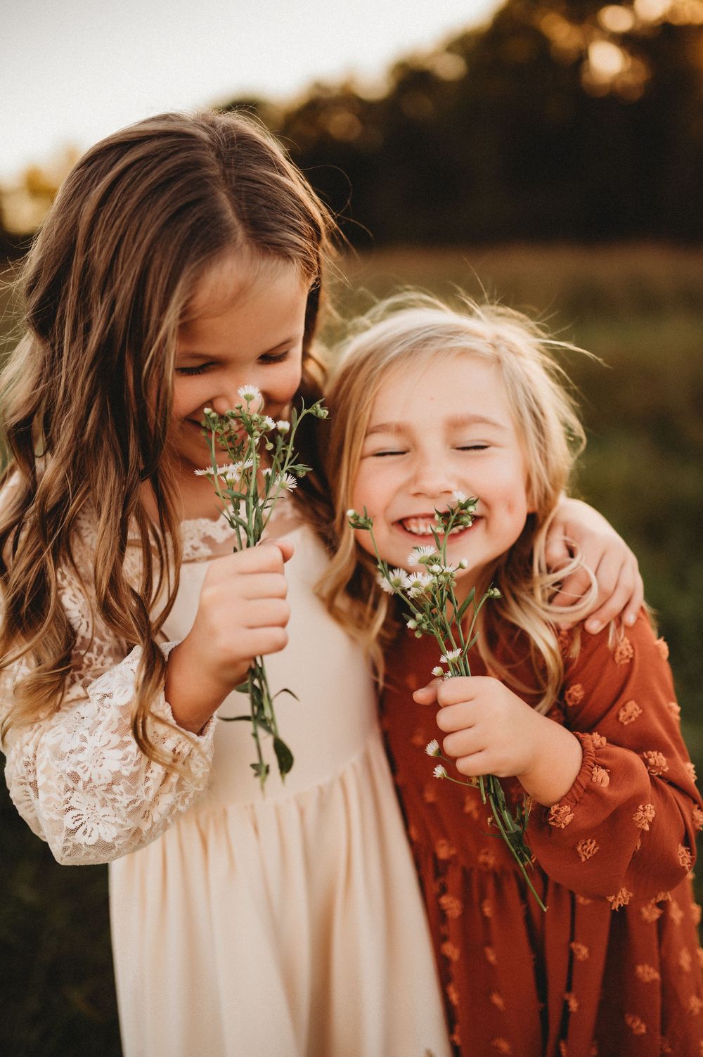 Two children sharing laughter while holding delicate wildflowers in golden sunset lighting.