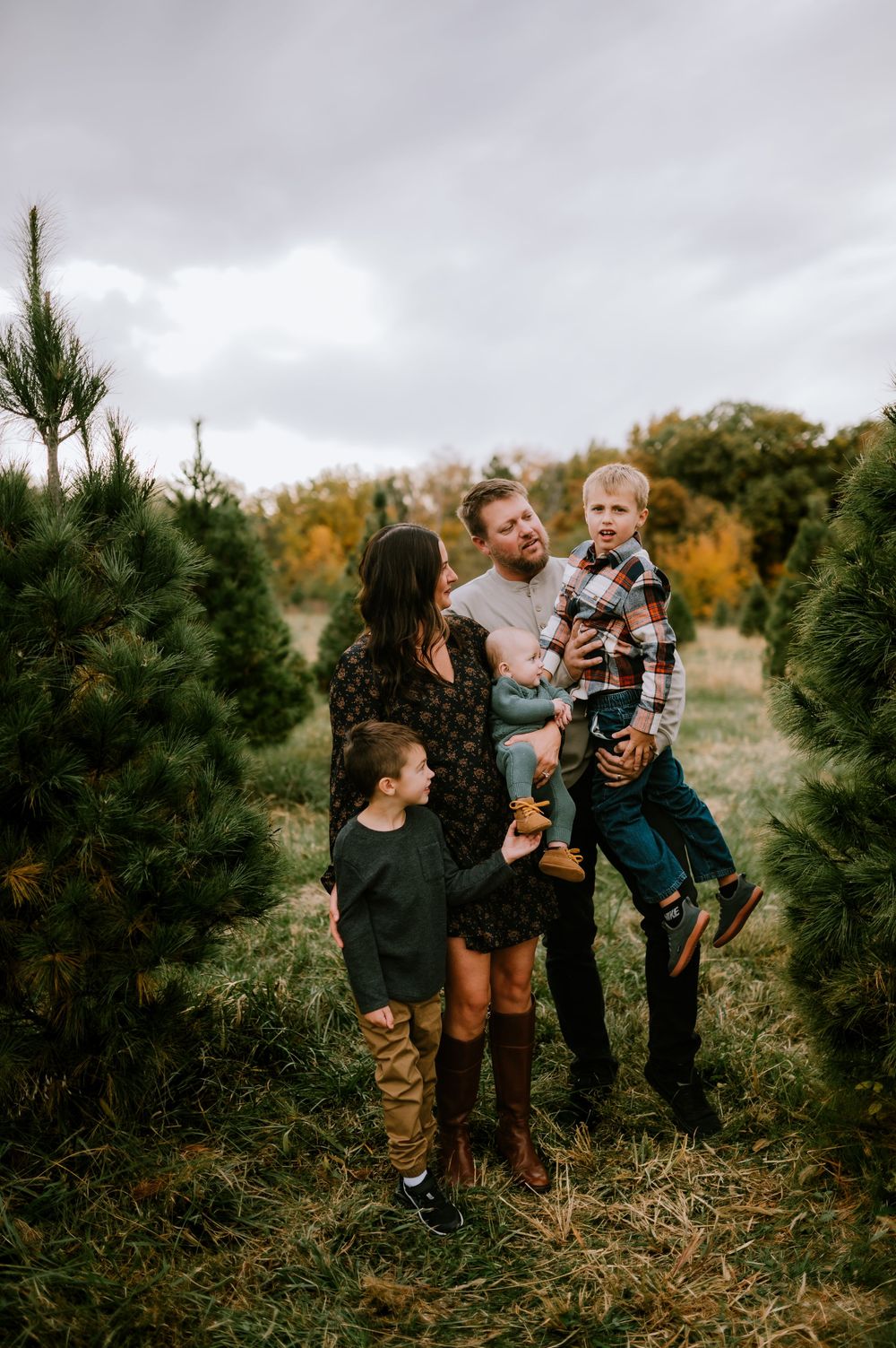 Family enjoying a fun moment together while walking through rows of evergreen trees at a Christmas tree farm.