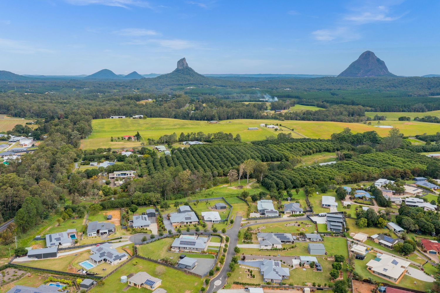 Panoramic aerial view of residential estate with iconic Glass House Mountains twin peaks backdrop in Queensland.