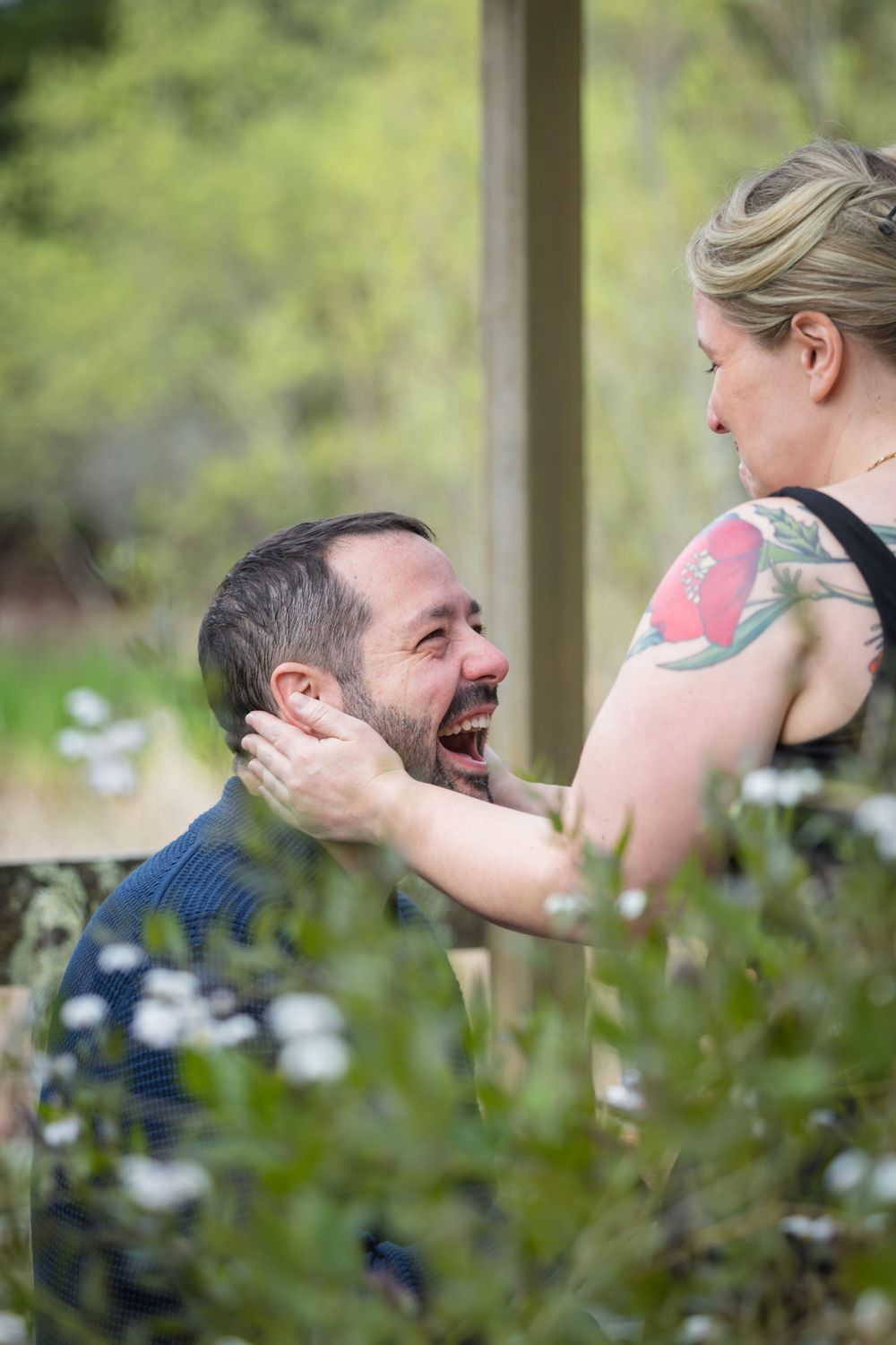 Two people share candid laughing moments in a garden setting with soft green foliage in the background.