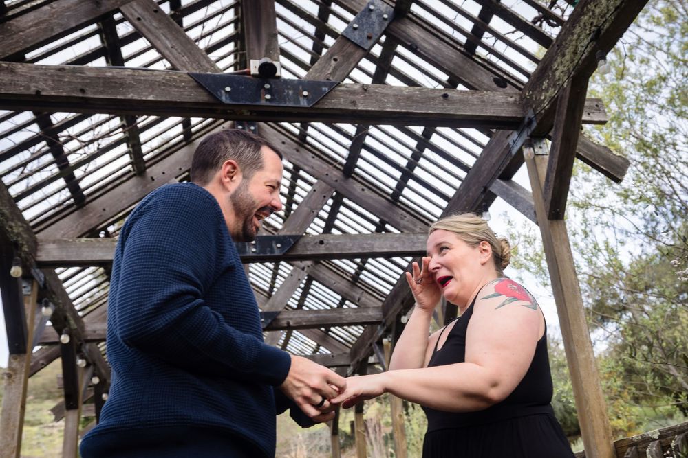 Couple shares intimate moment under wooden pergola structure in garden setting.