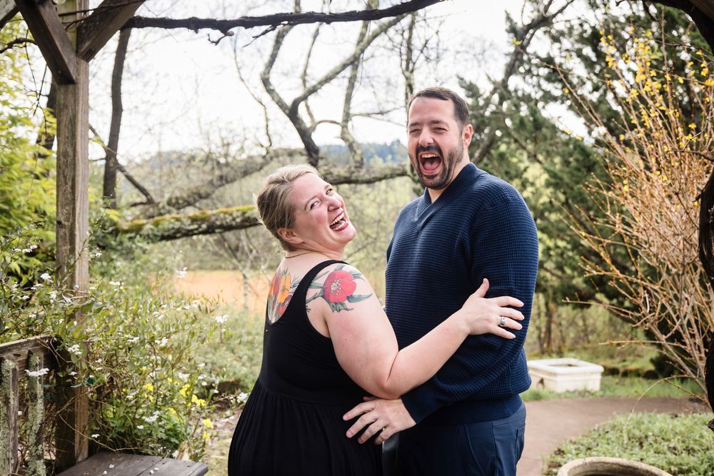 A joyful couple shares candid laughter during their engagement photoshoot in a natural outdoor setting.