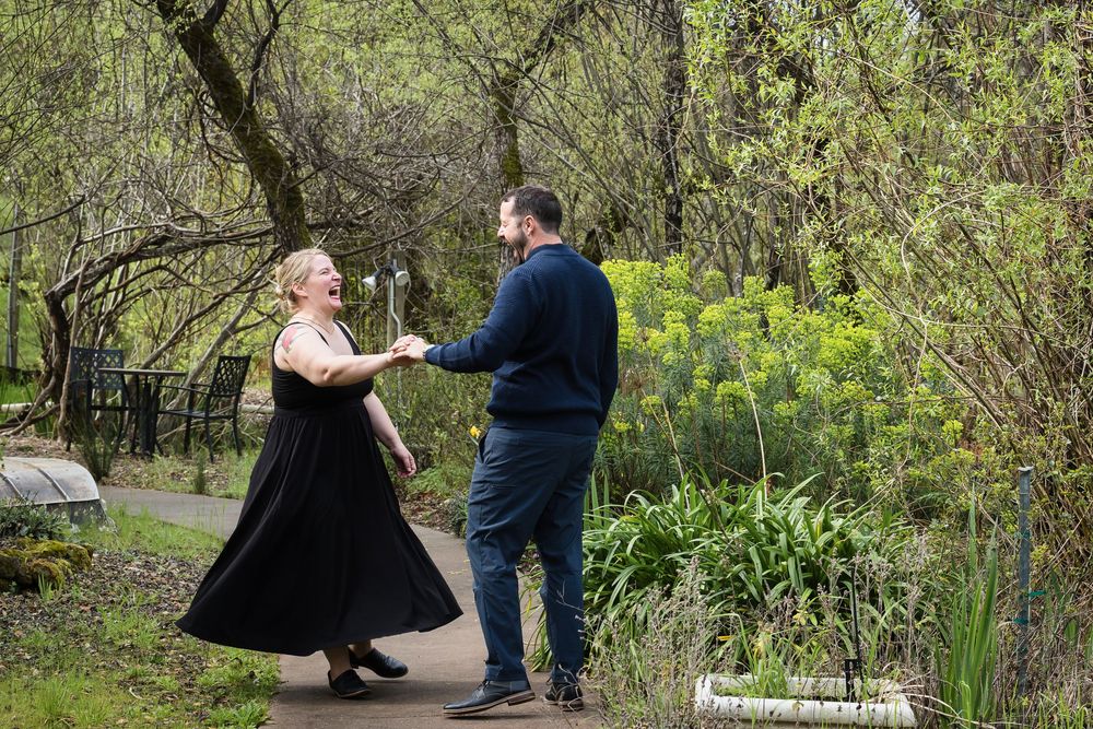 A couple dances together on a garden path surrounded by spring greenery and yellow wildflowers.