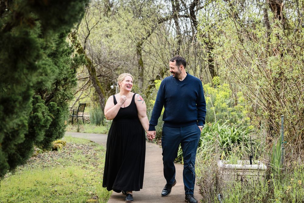 A couple walks hand in hand along a garden path surrounded by lush greenery on a spring day.