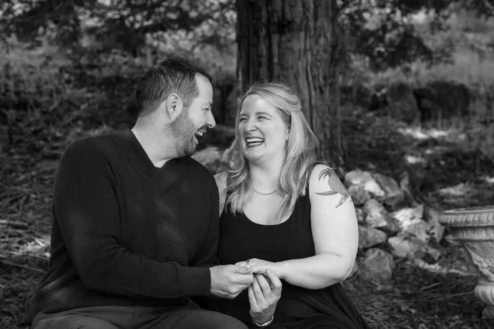 A couple embraces and laughs together during an outdoor black and white photo session.