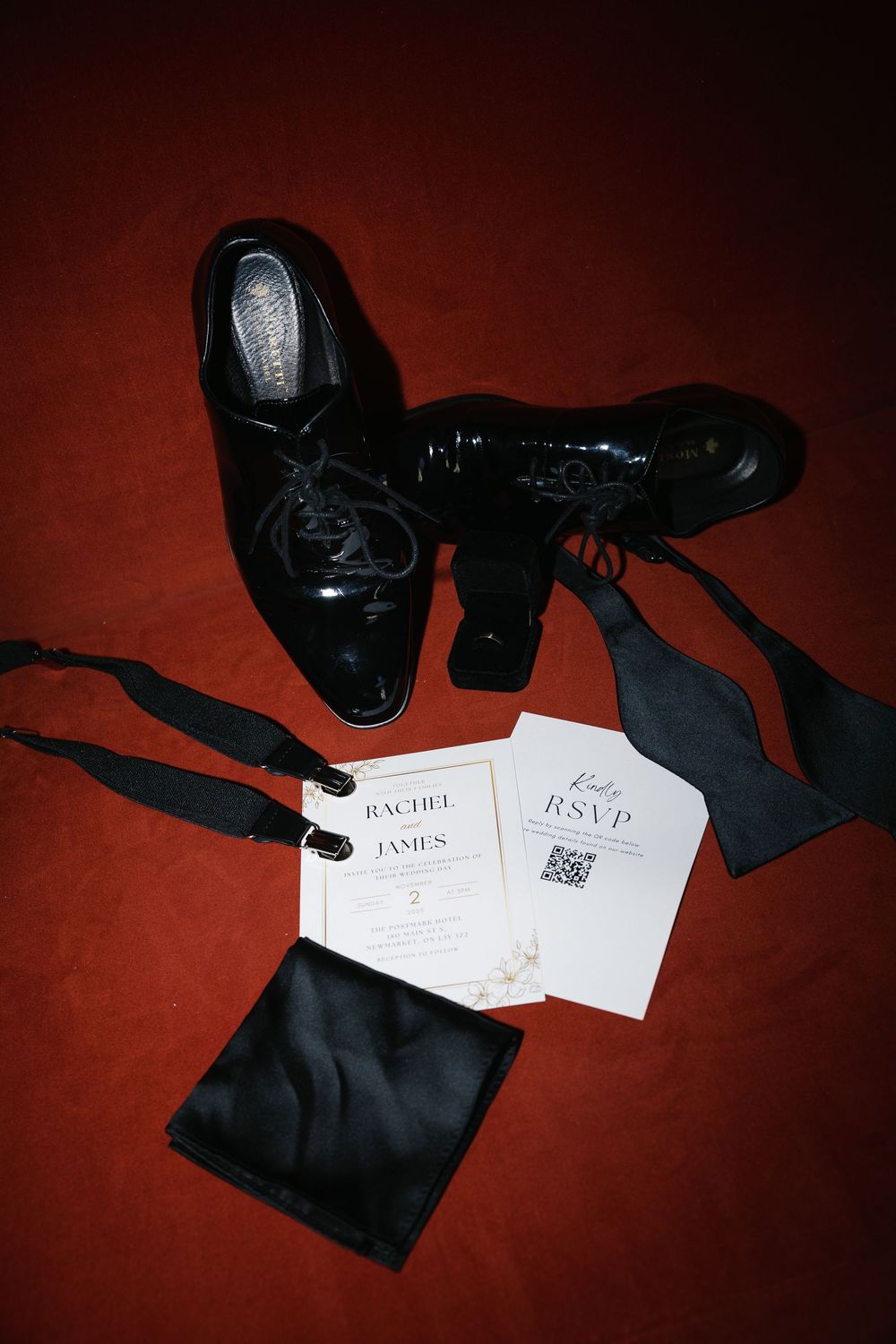 Black formal accessories and RSVP cards arranged artistically on a deep red background.