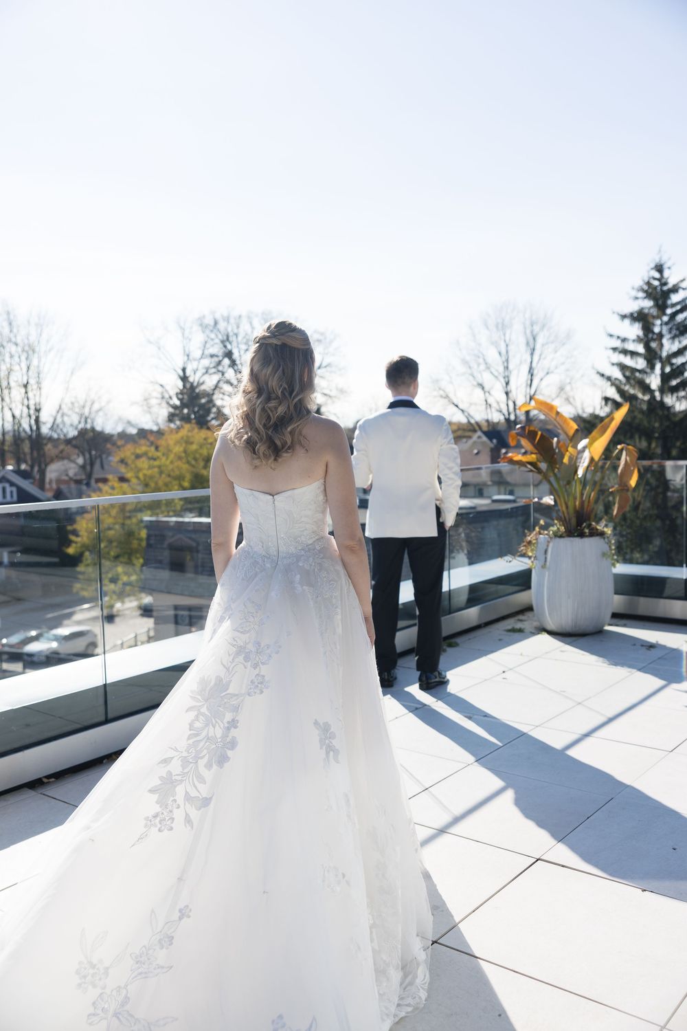 A couple shares a private moment on a rooftop terrace with glass railings and autumn trees in the background.