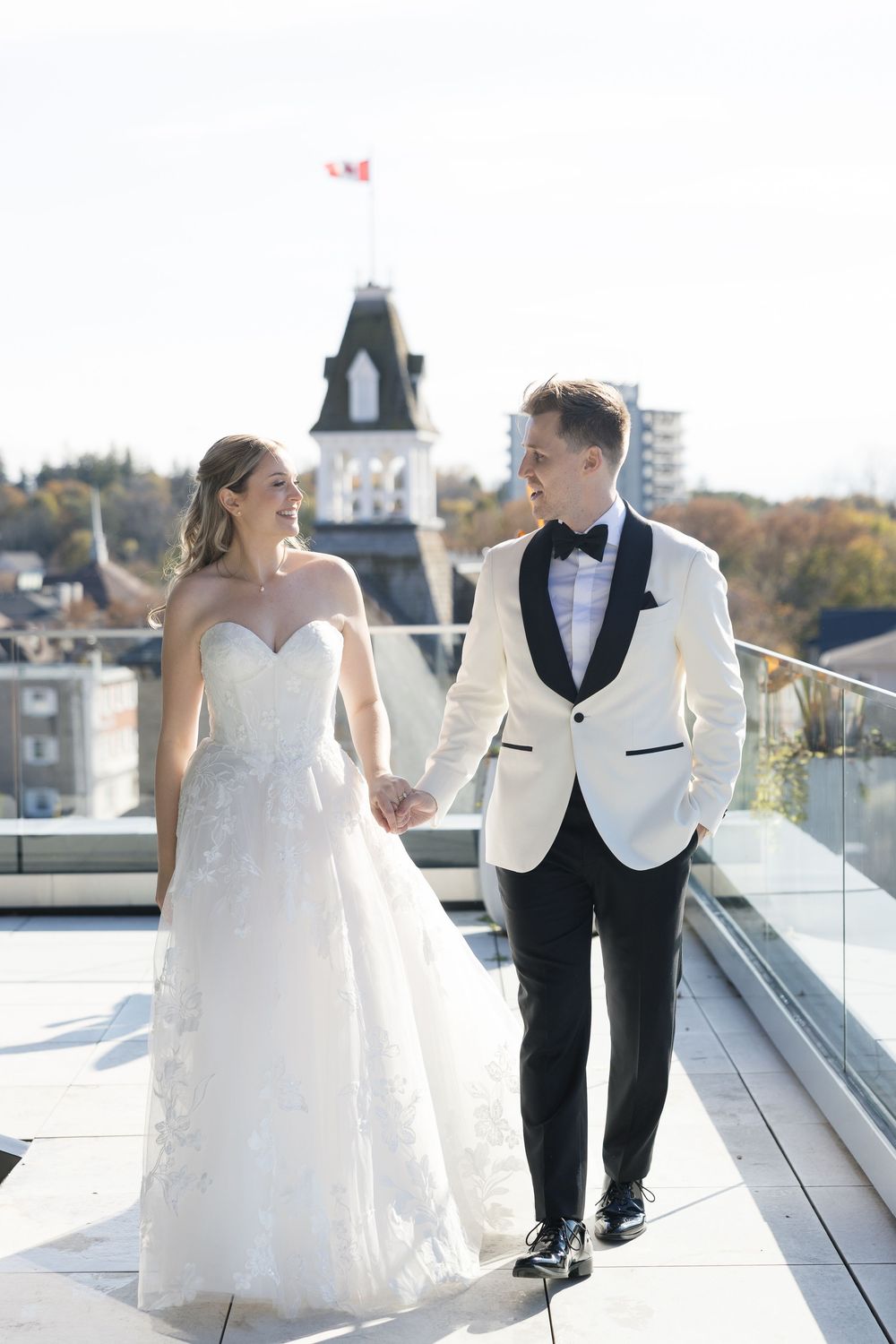 A romantic wedding couple poses together on a rooftop terrace with city views in the background.