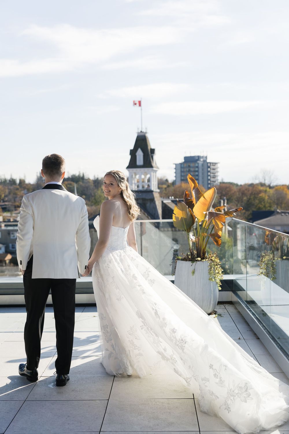Wedding couple poses on rooftop terrace with cityscape and Canadian flag in background.