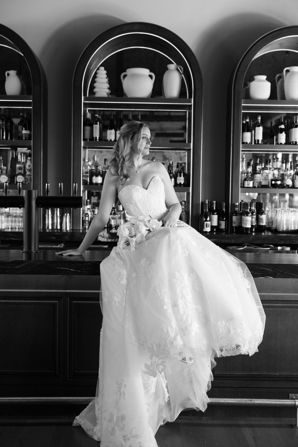 A wedding couple dances in front of an elegant bar with arched alcoves in black and white photography.