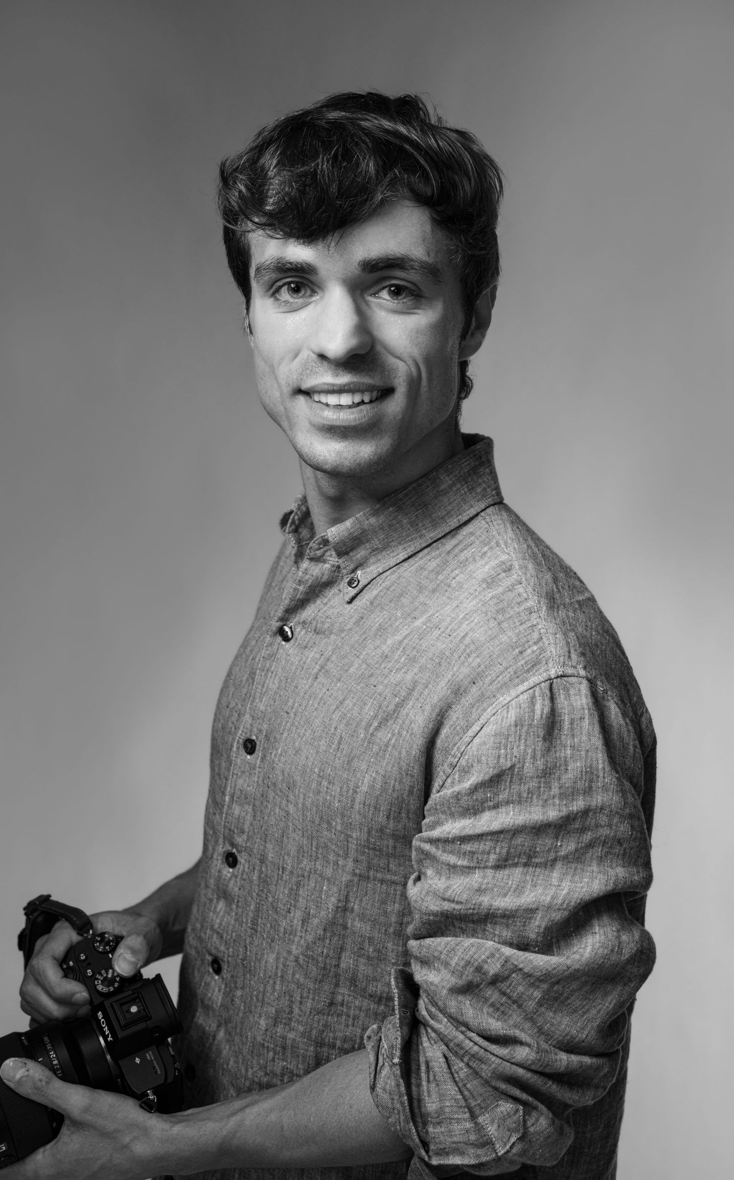 A series of black and white portraits showing someone wearing a gray button-up shirt while holding a camera.
