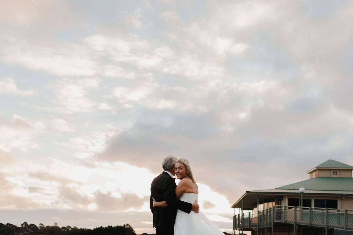 A romantic sunset wedding photo of a couple embracing by a lake with a flowing white dress.