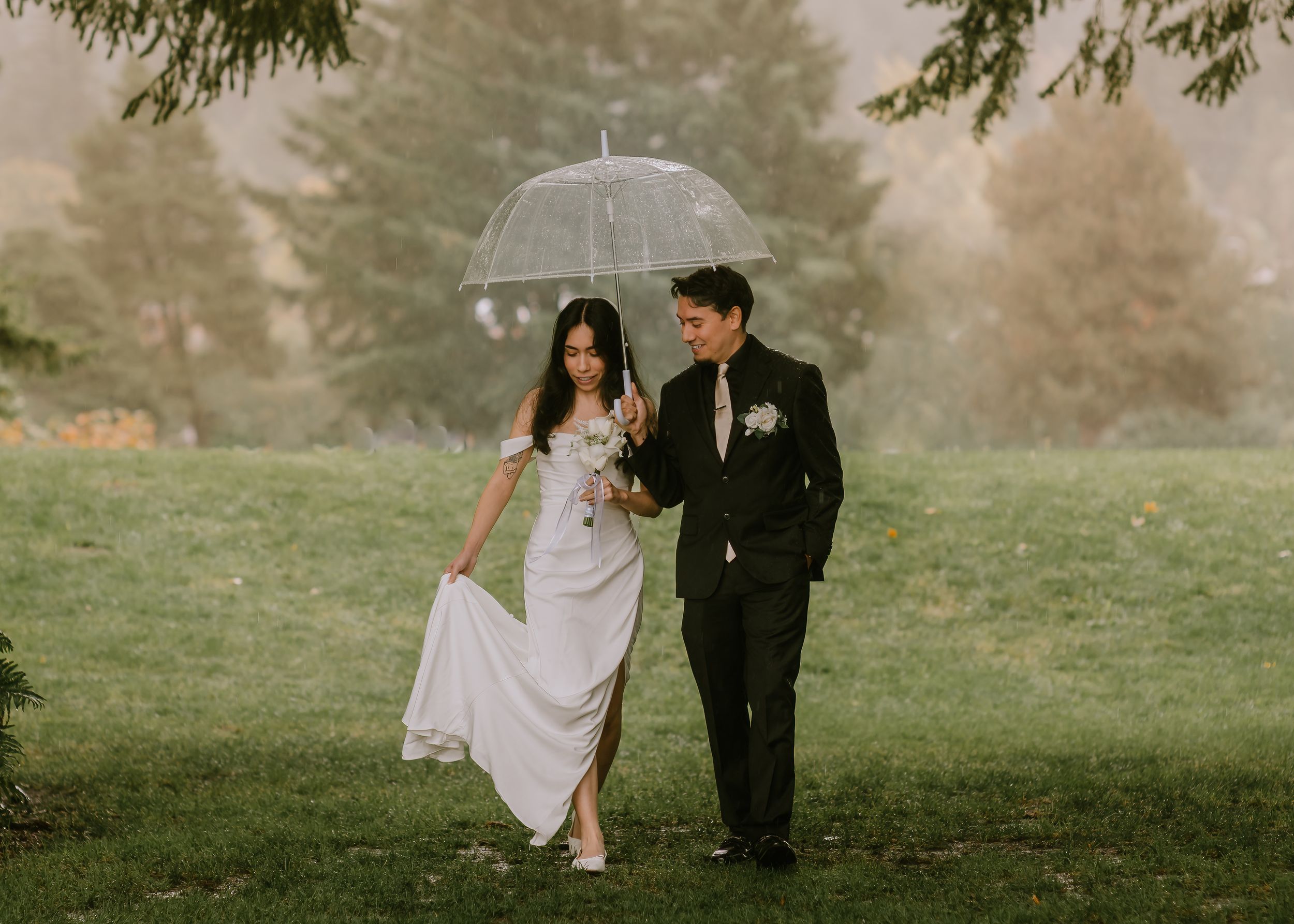 A romantic wedding couple sits together in a misty green field during a dreamy outdoor photo session.