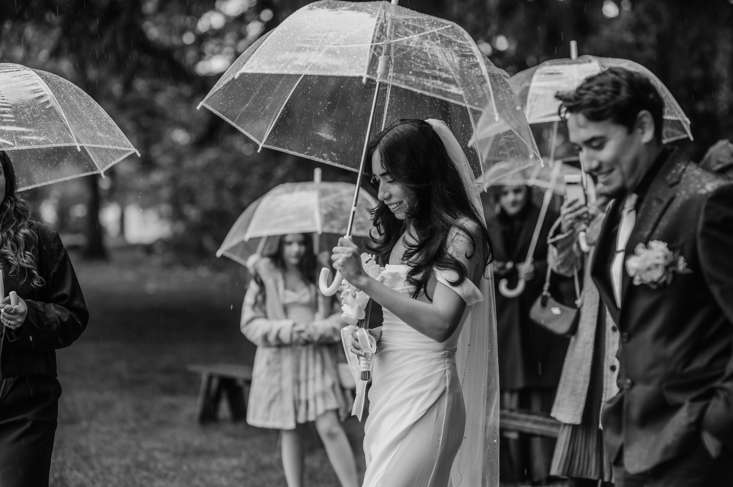 A black and white photo montage of wedding guests holding umbrellas during an outdoor celebration.