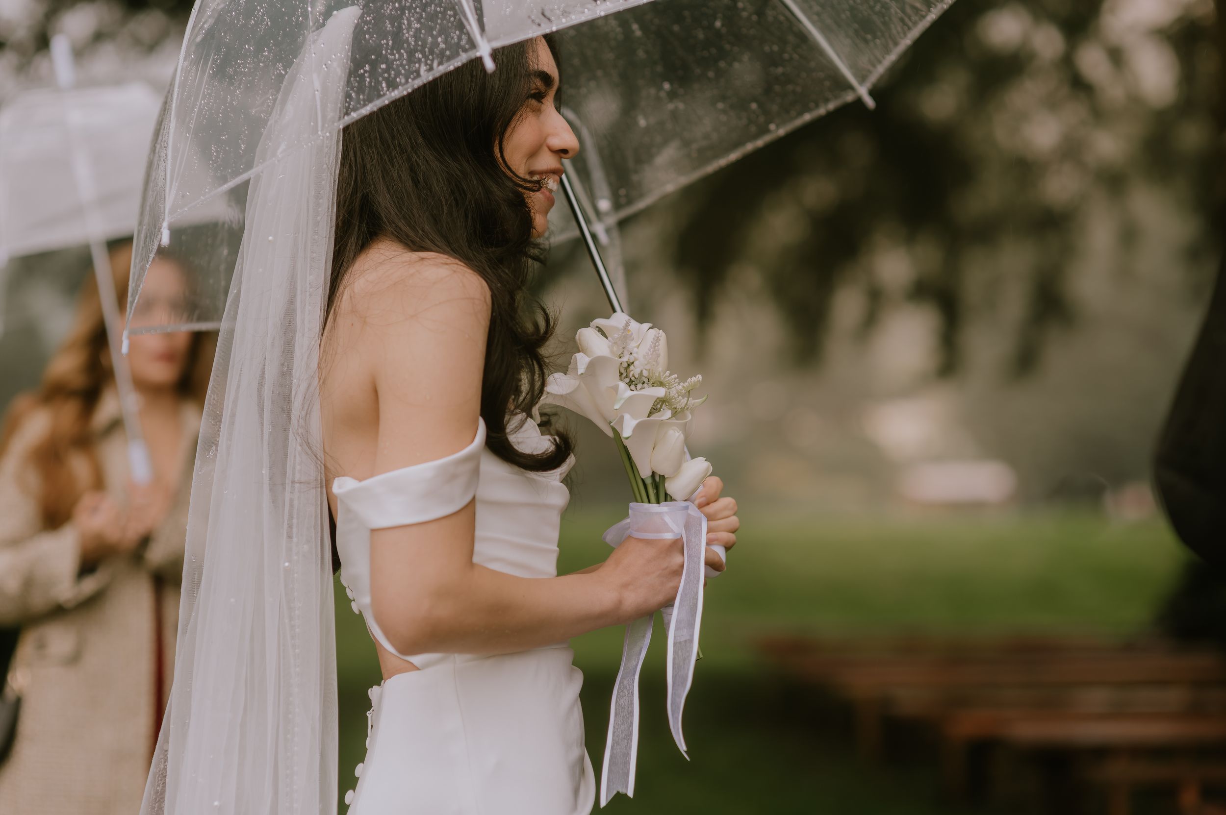 A bride holds a delicate white bouquet during an outdoor wedding ceremony in a garden setting.