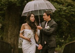 A couple shares a clear umbrella while walking together on their rainy wedding day in a romantic outdoor setting.