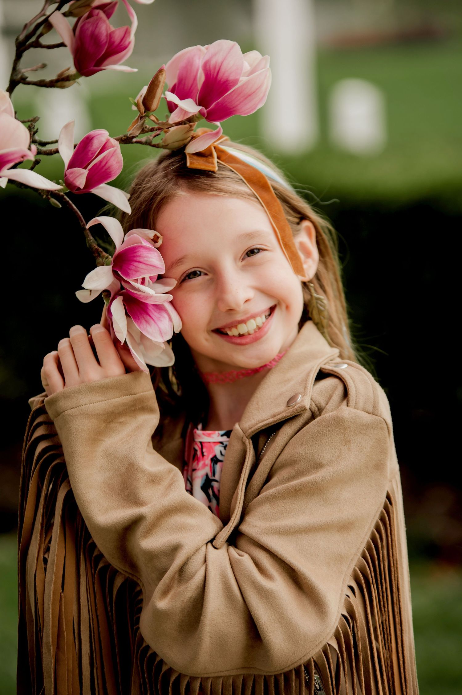 Beautiful pink magnolia flowers frame a joyful moment in a fringed suede jacket against a soft green background.