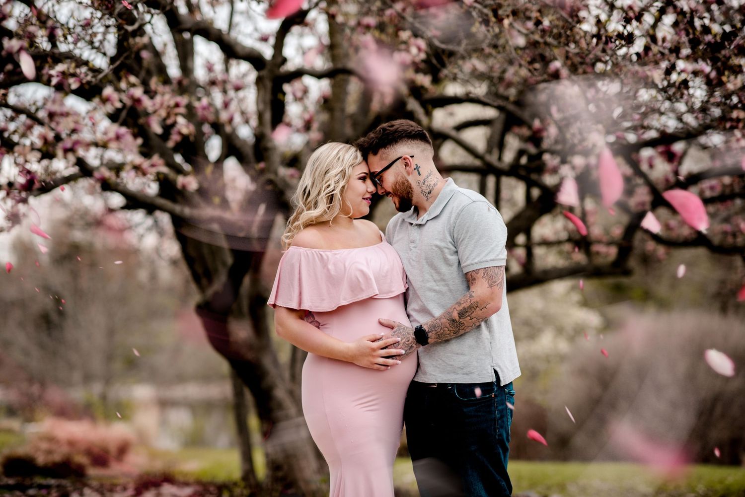 A couple embraces under blooming pink cherry blossom trees during a romantic spring photoshoot.