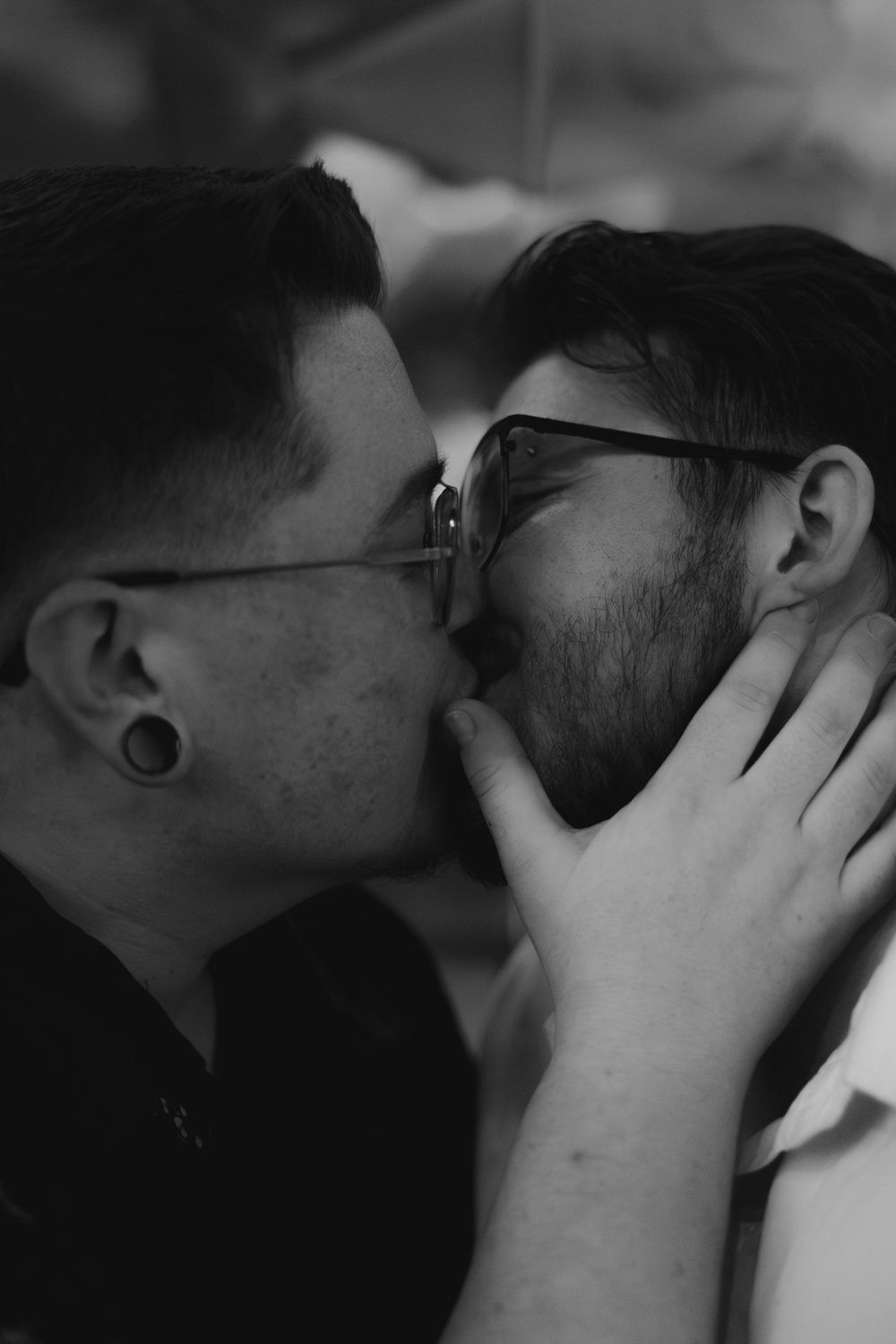 A black and white intimate portrait of two people sharing a tender kiss while one gently holds the other's face.