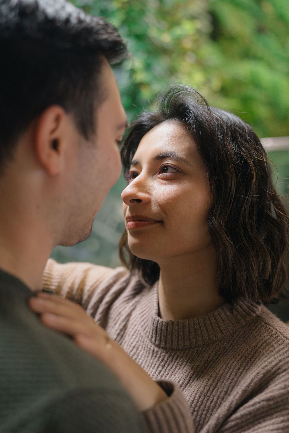 A romantic couple in cozy sweaters sharing an intimate moment outdoors with soft natural lighting.
