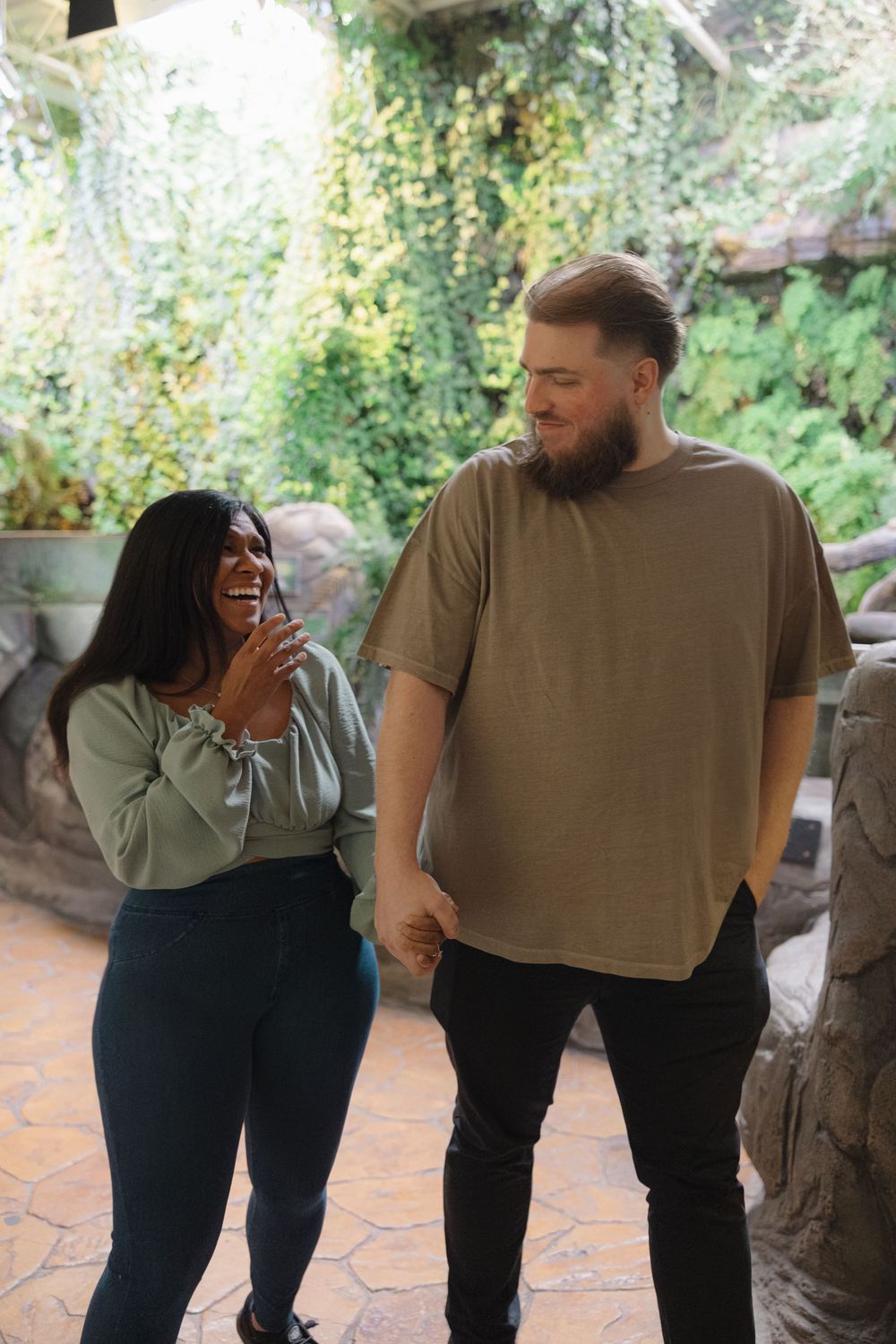 A happy couple shares a candid laughing moment together while holding hands in a lush garden setting.