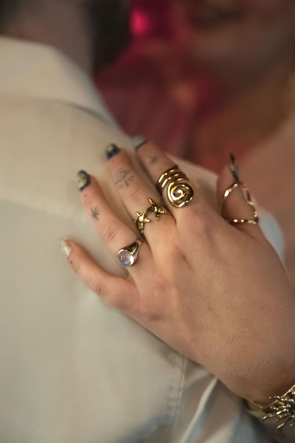 Multiple delicate gold and silver rings with unique designs are displayed on a person's hand against a blurred background.