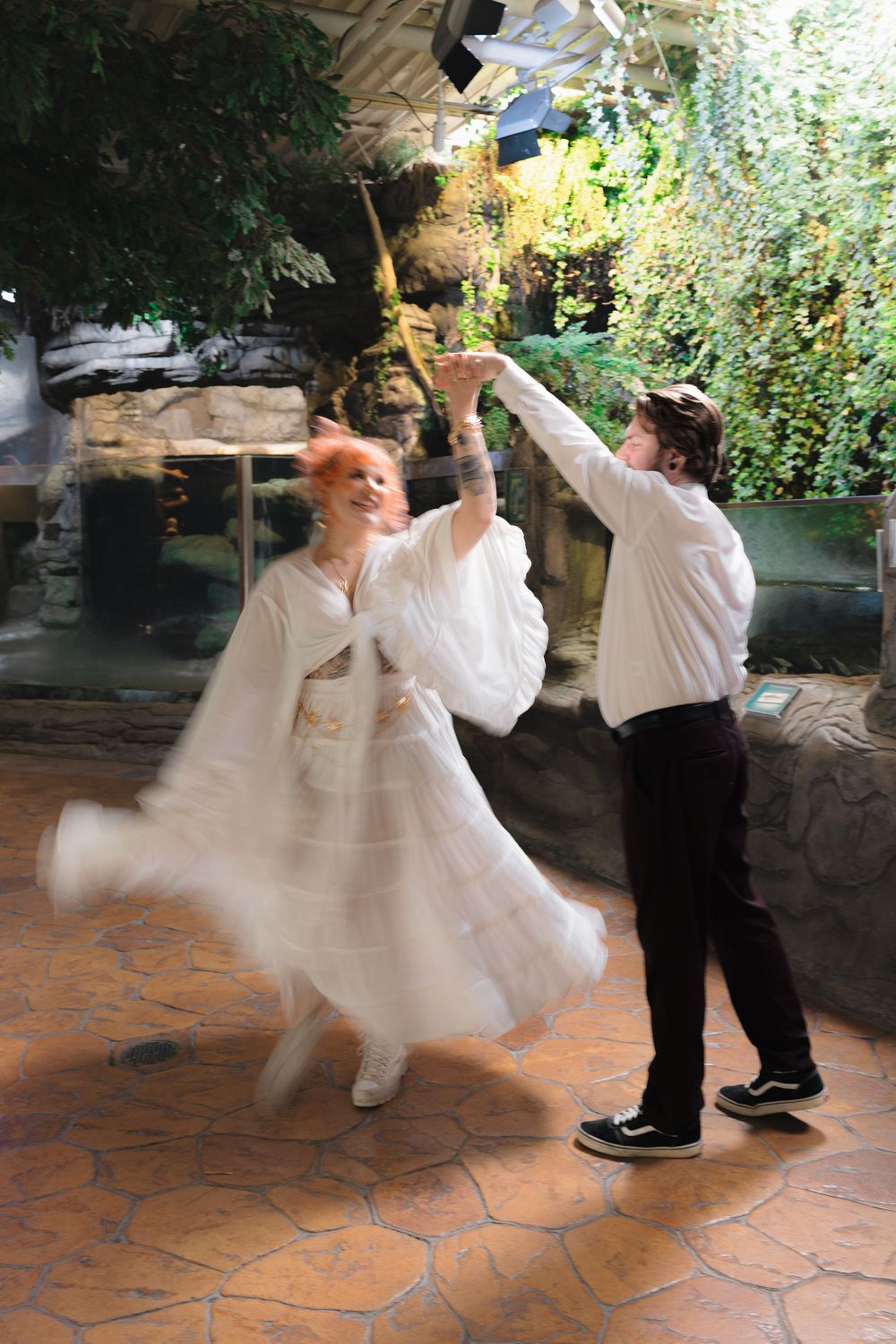 A couple dances energetically on a tiled patio, with the person in white twirling in a flowing dress.