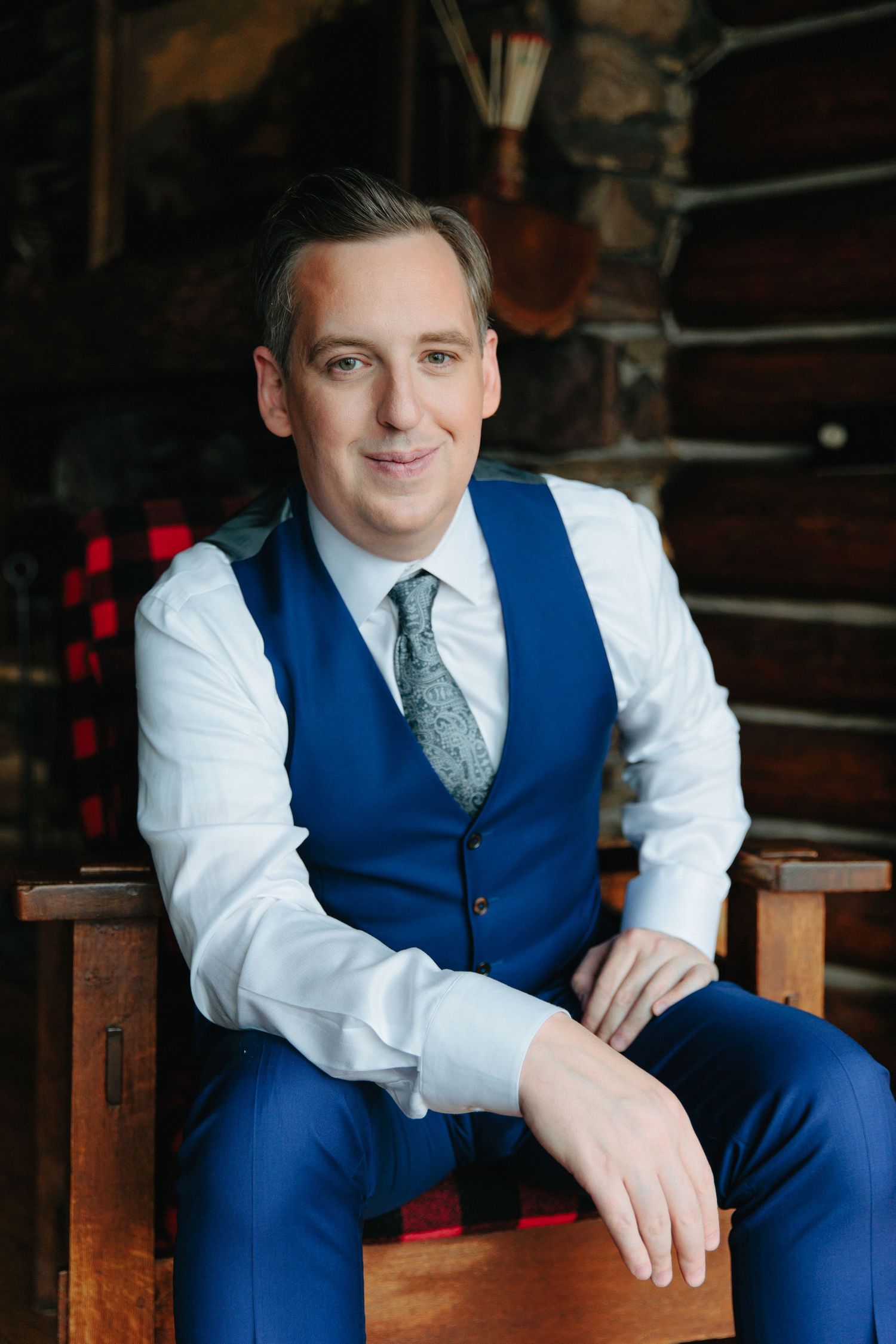 Wedding attire featuring blue vest, white shirt, and patterned tie in rustic indoor setting.