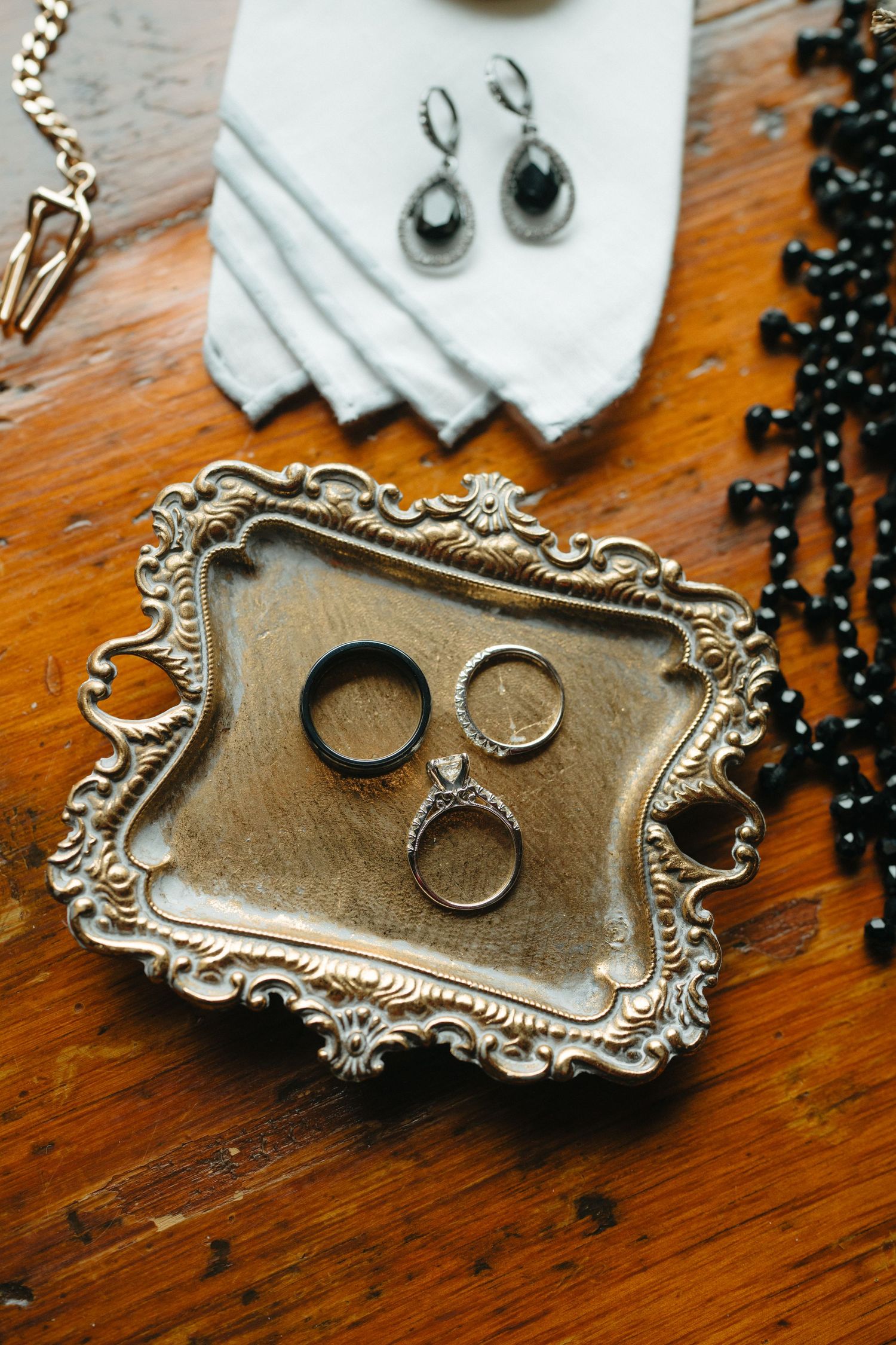 Wedding jewelry and rings arranged on an ornate vintage silver tray with black beaded accents.