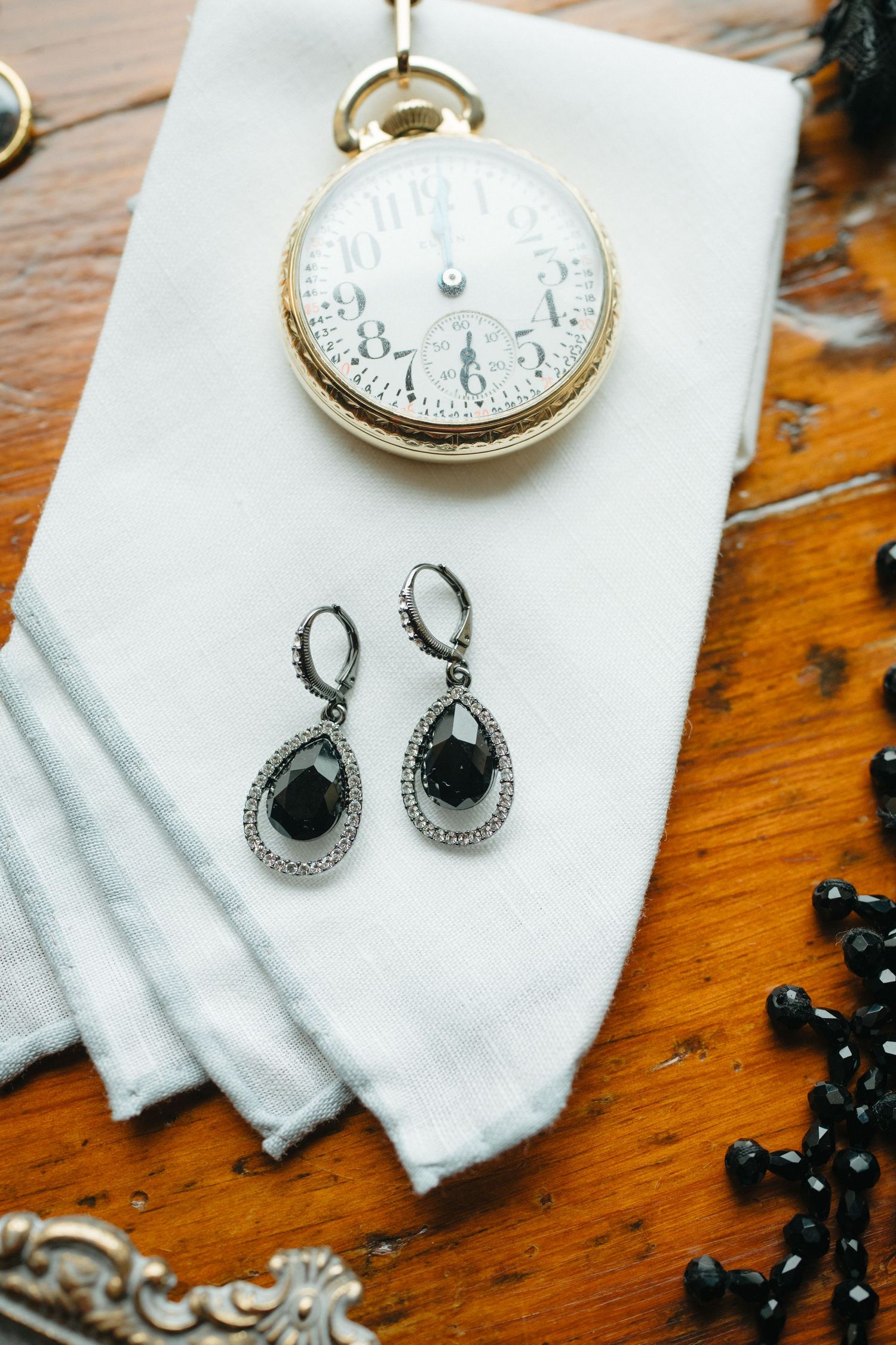Vintage pocket watch and black teardrop earrings displayed on white fabric.