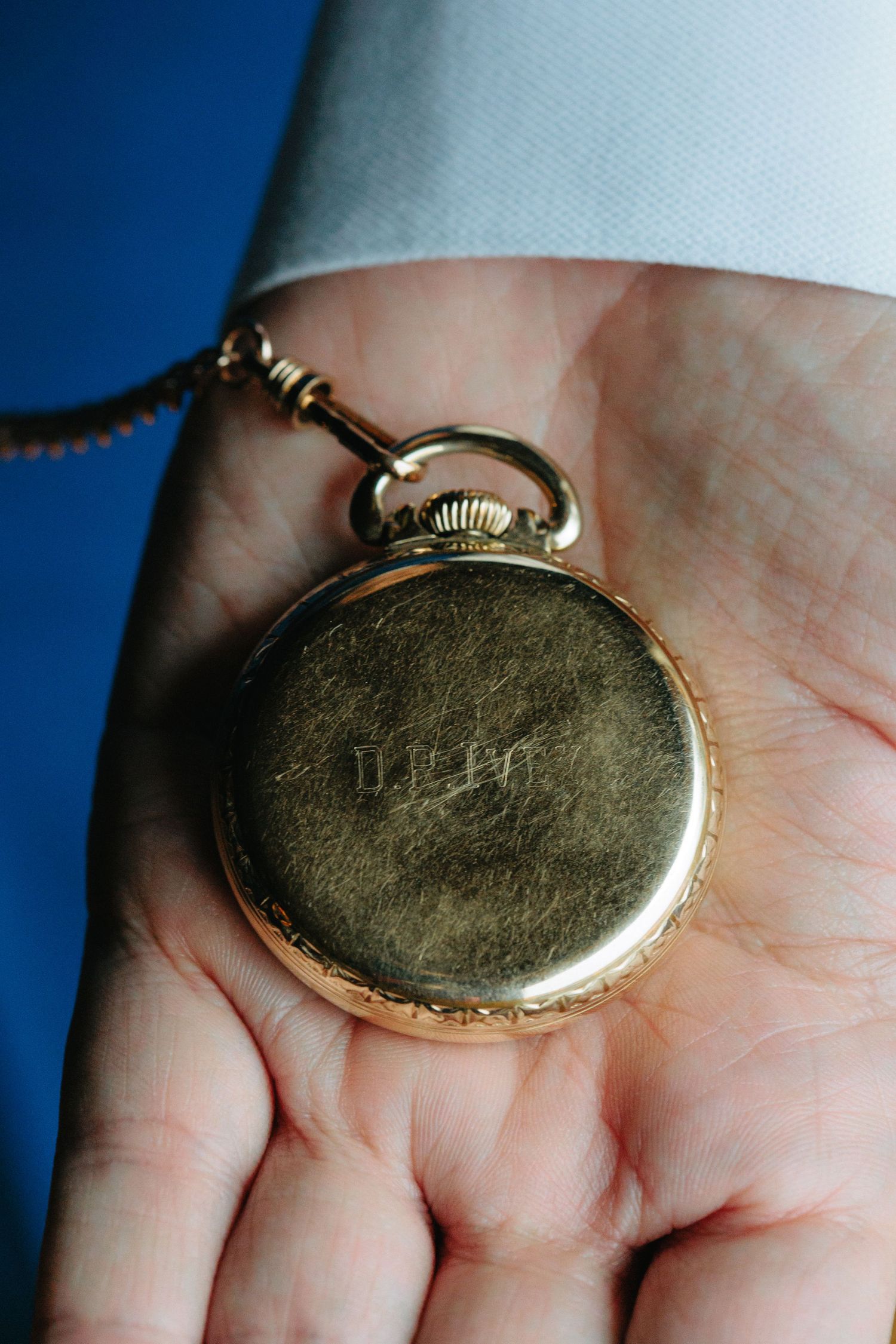 A vintage gold pocket watch rests in an open palm against a blue background.