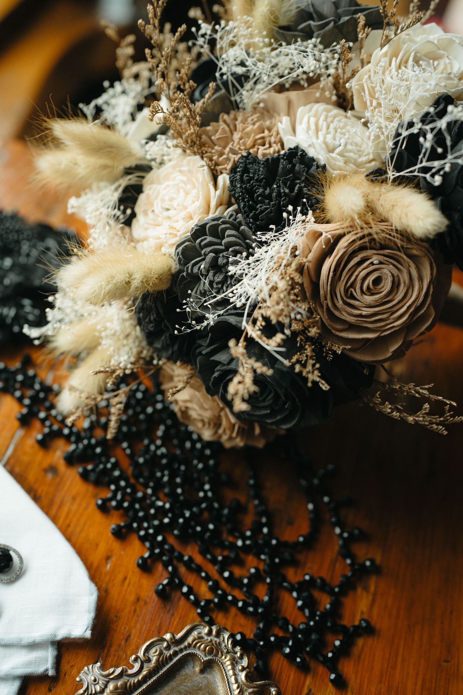 Dried floral arrangement with brown roses and white baby's breath on wooden surface with black beads.