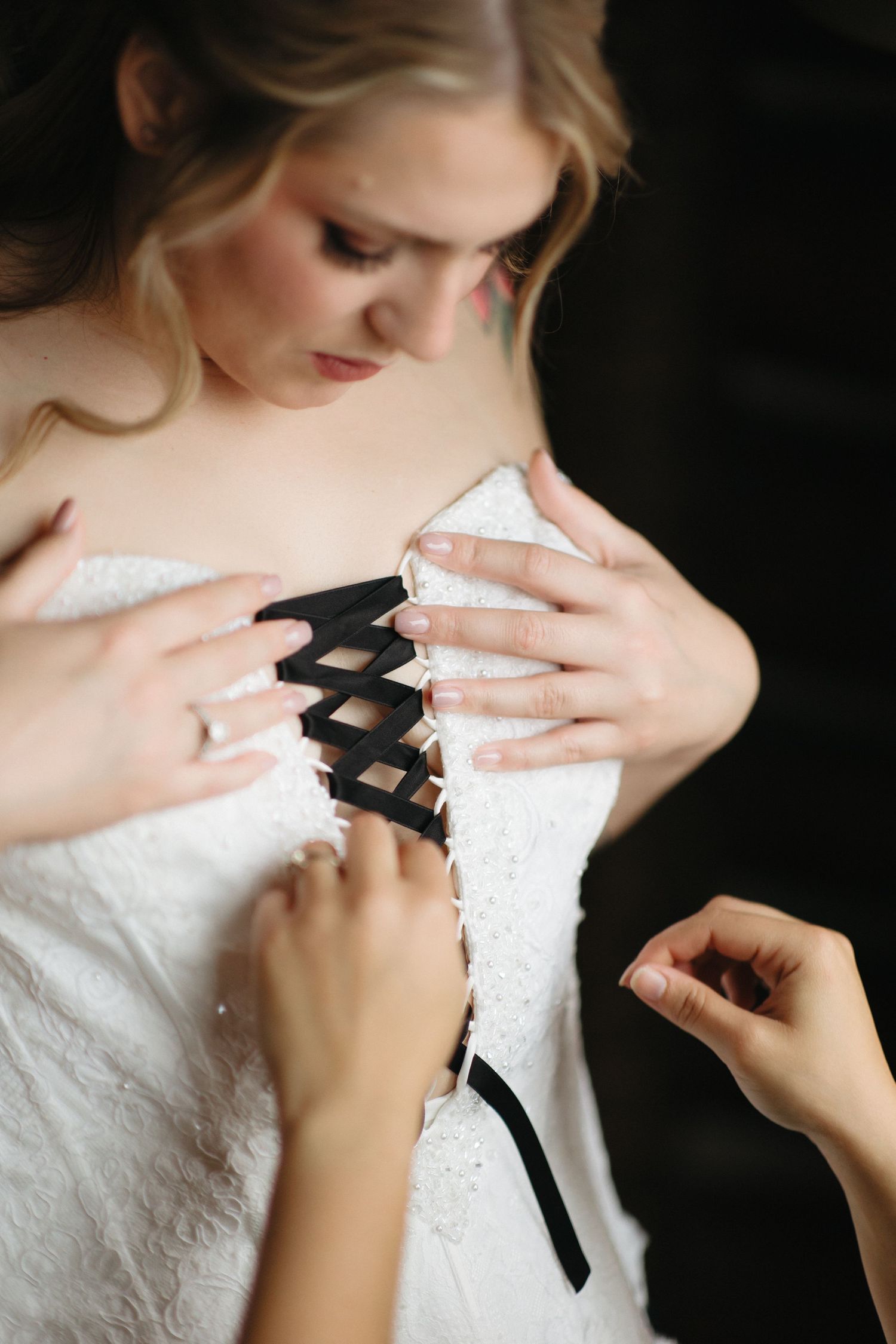 Close-up of hands lacing up a white corset wedding dress.