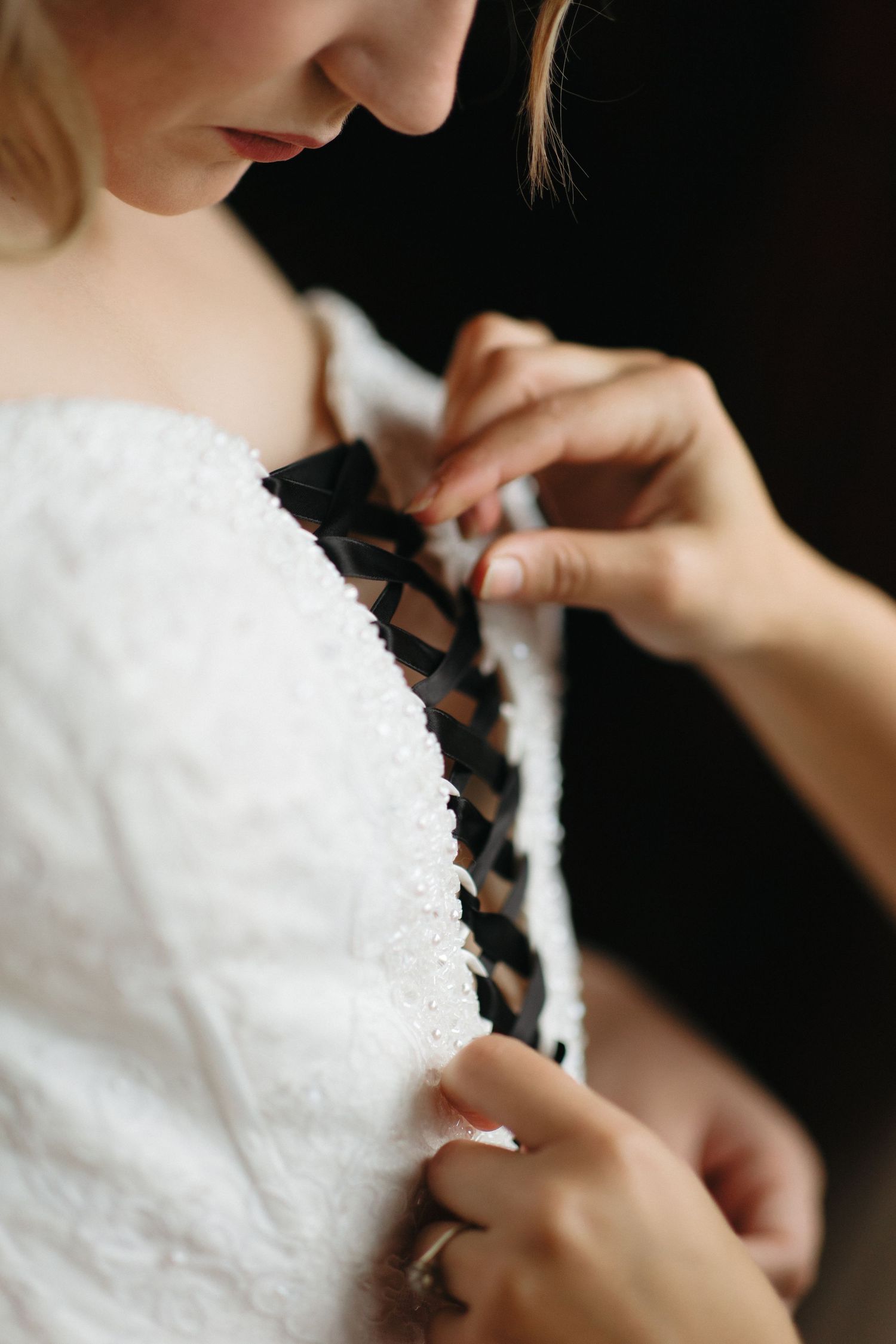 Close-up view of someone helping with a white wedding dress, showing intricate details and adjustments being made.