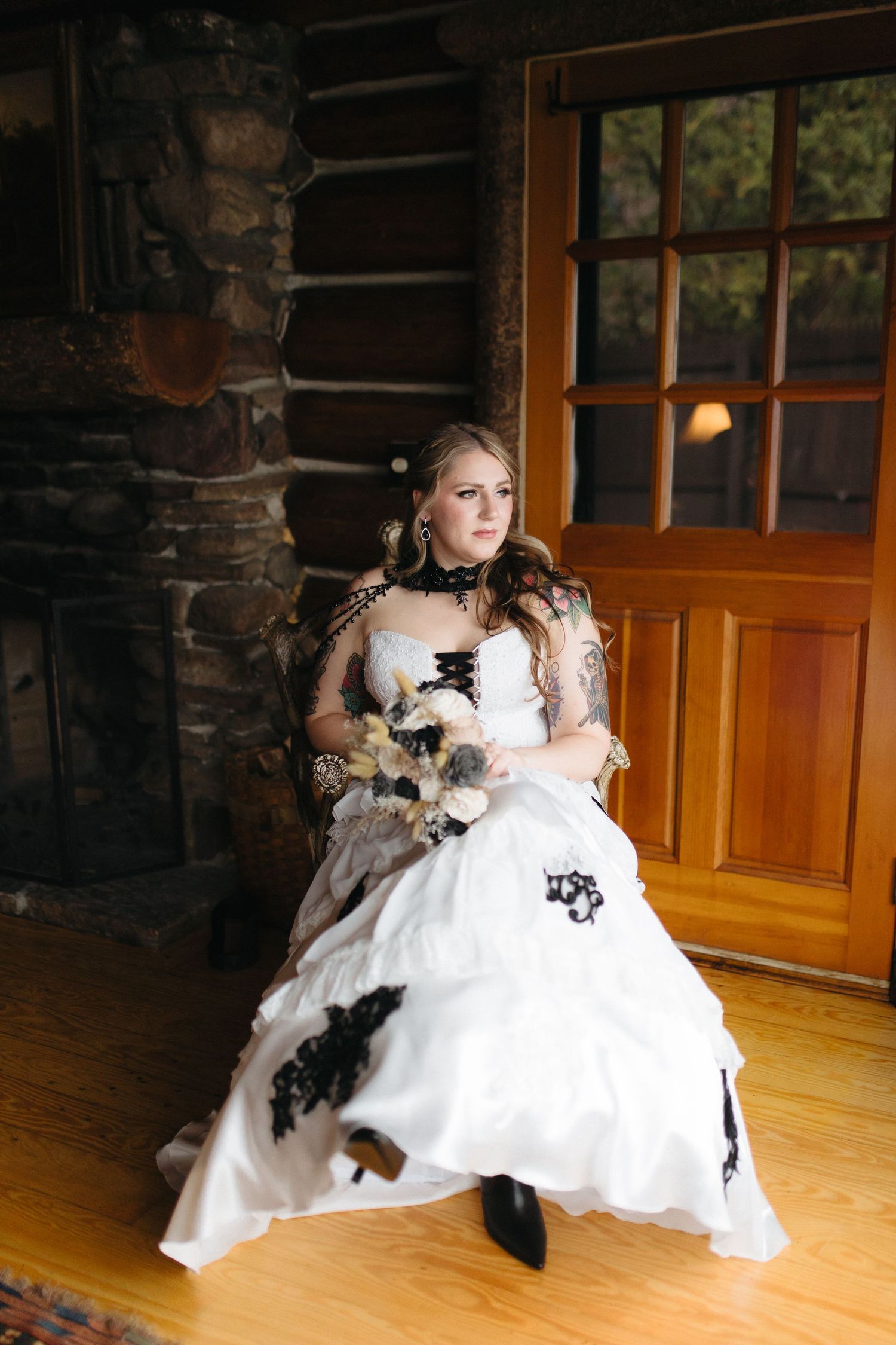 A bride in a white gown with black accents sits in a rustic cabin setting.