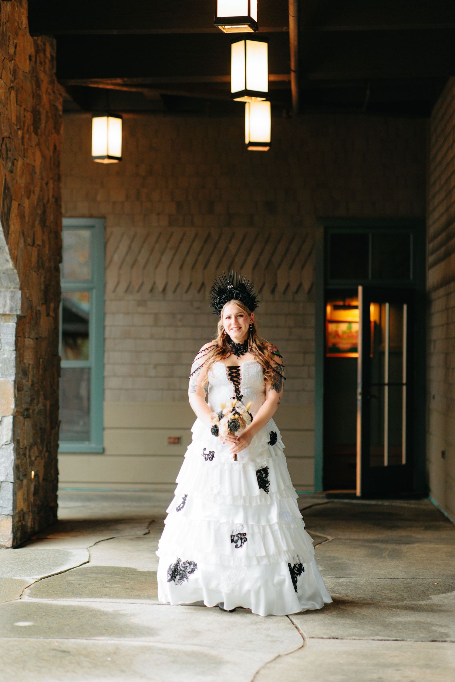A bride in a white dress with black butterfly accents twirls playfully under rustic wooden beams and pendant lights.