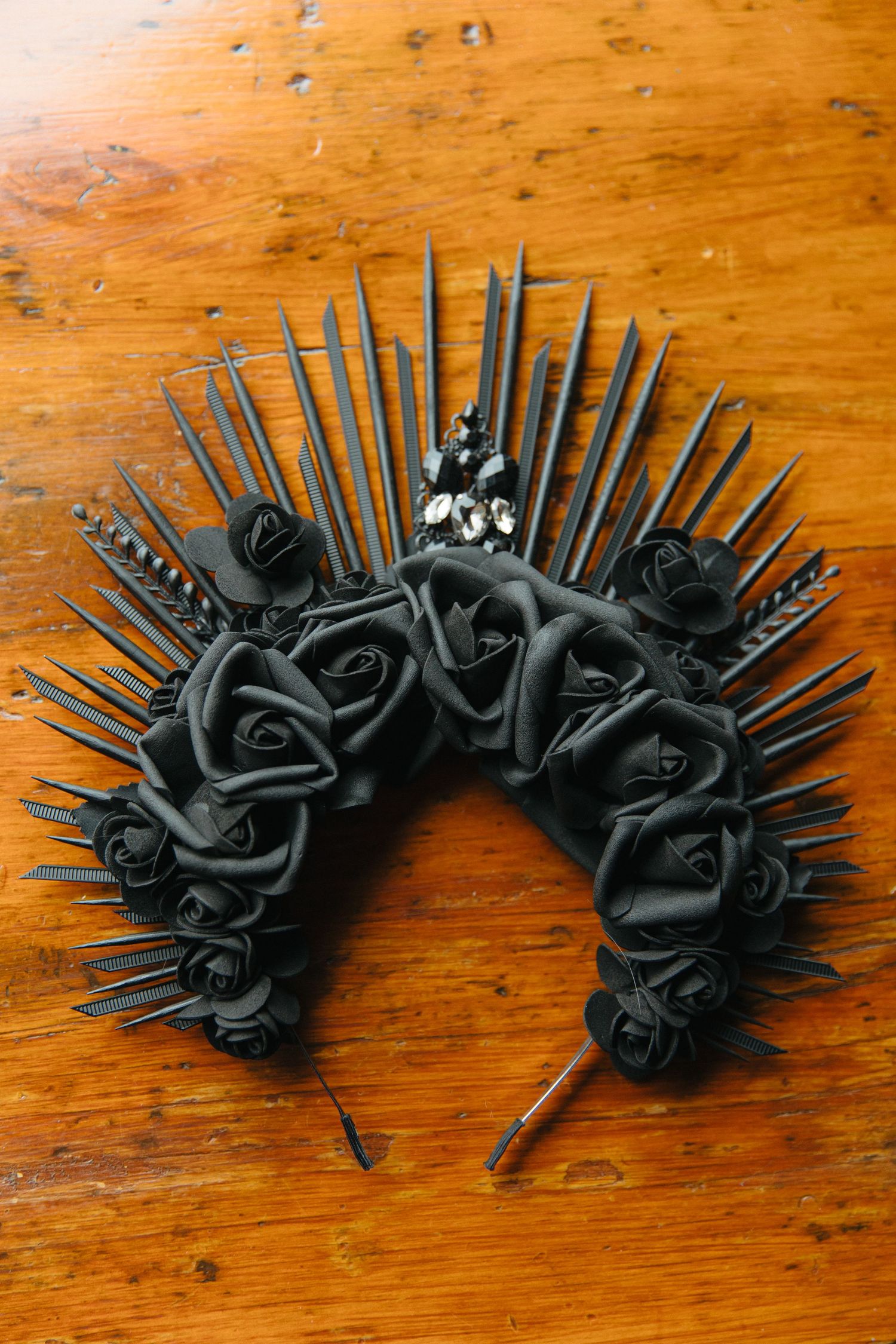 Gothic black rose crown headpiece with metal spikes arranged in a dramatic semicircle on wooden surface.