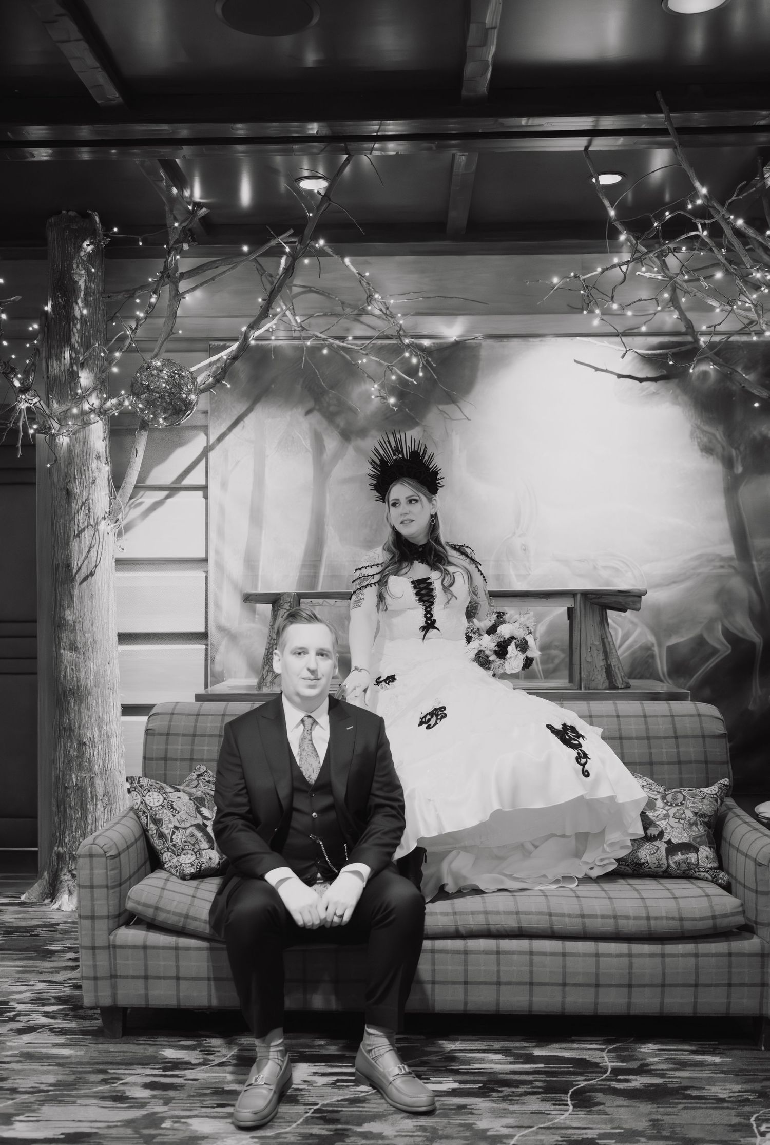 A black and white vintage photograph showing a person sitting alone on a couch in formal attire.