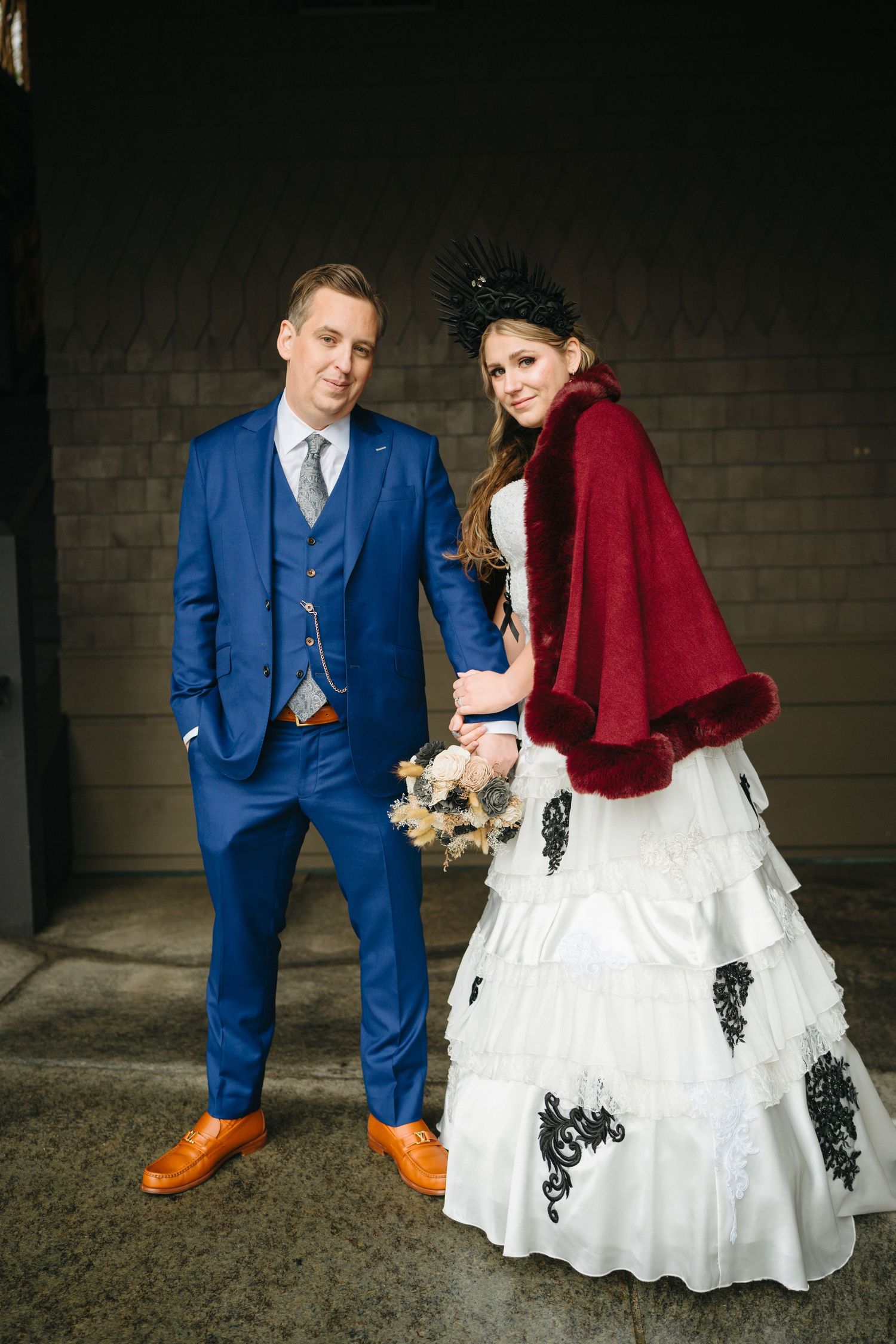 A couple in formal wedding attire, with the groom wearing a bright blue suit and orange shoes, pose together for photos.