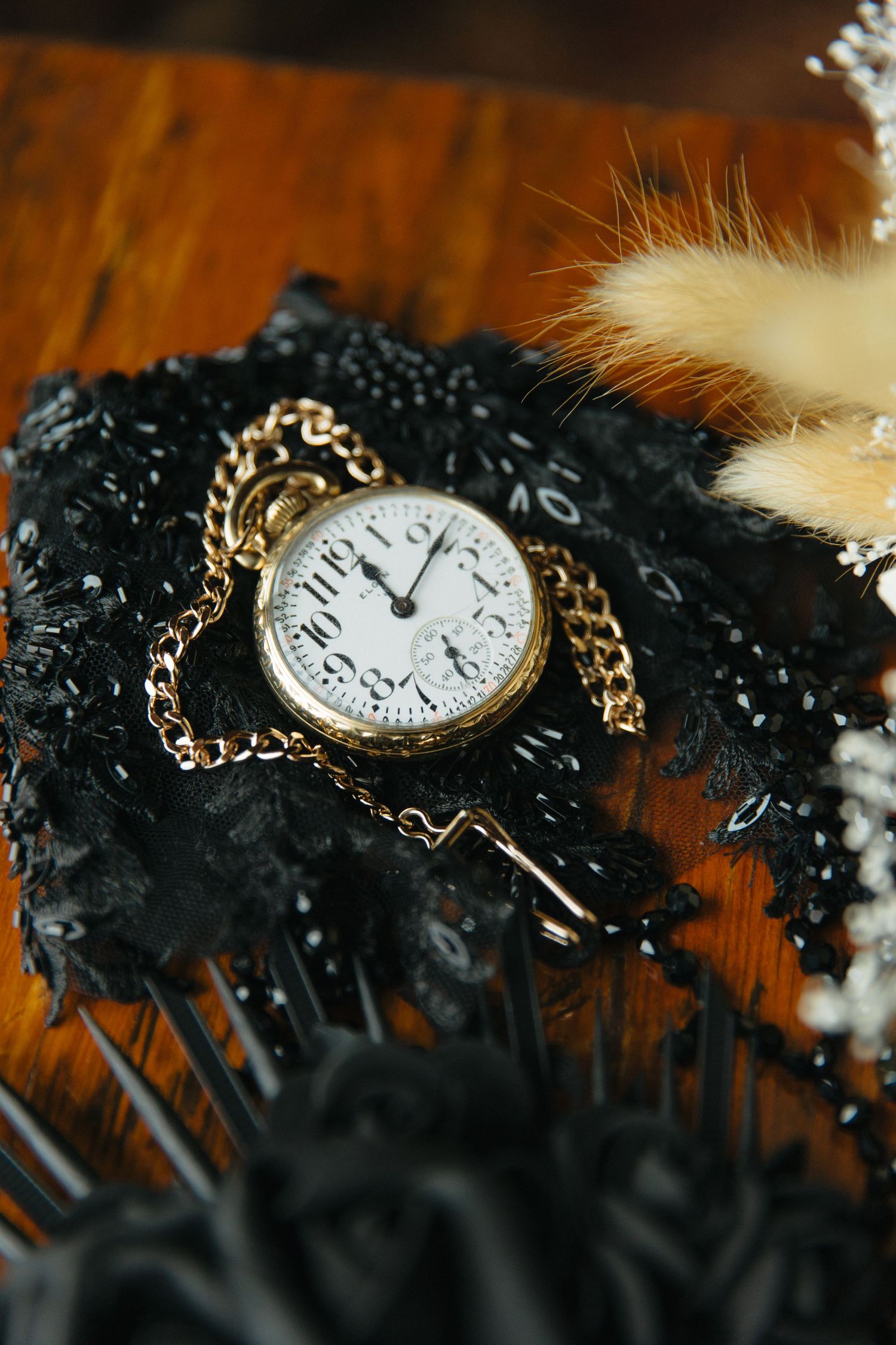 Antique gold pocket watch with chain resting on black lace fabric against wooden surface.